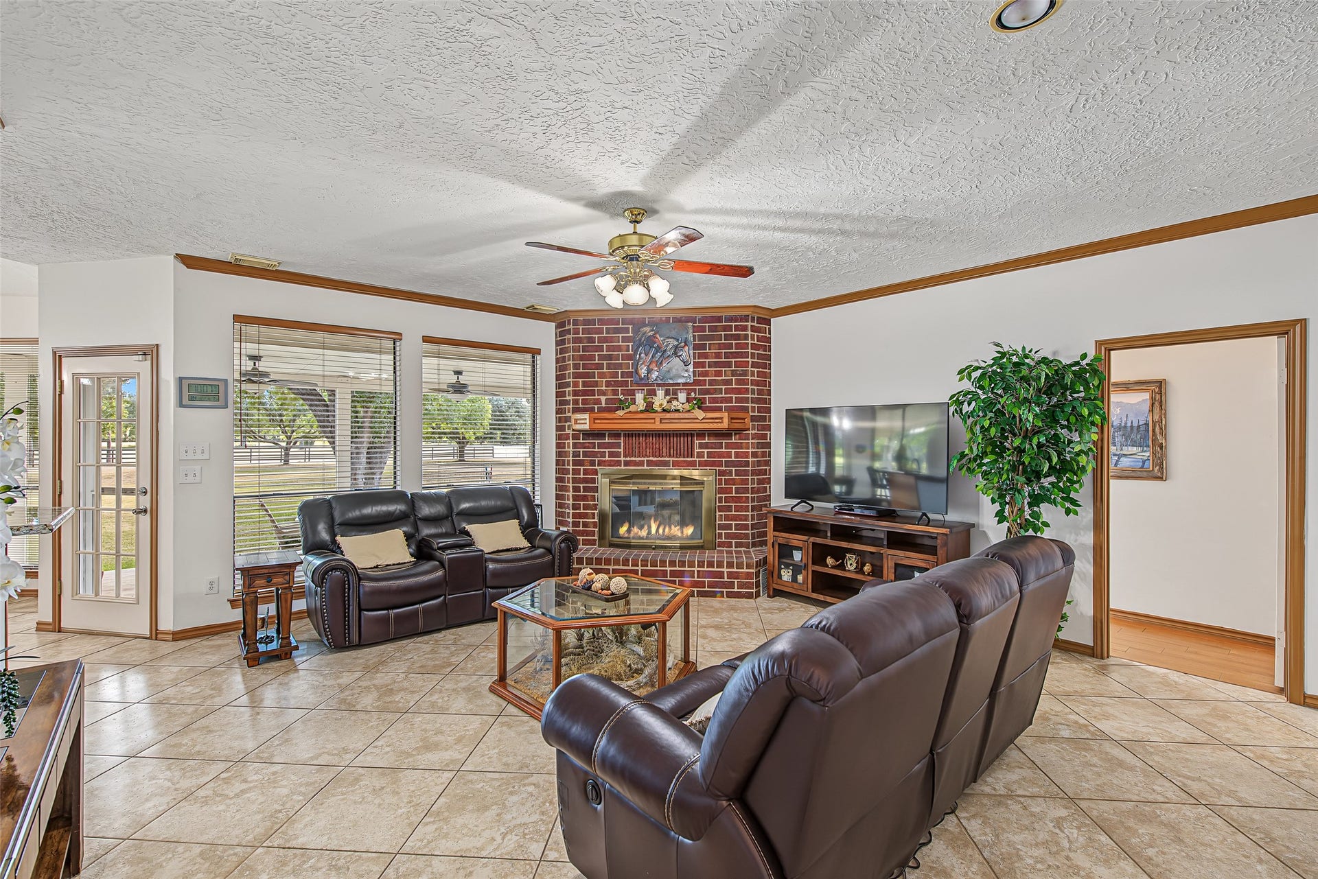 1345 Peach Ridge Road, Brookshire, TX 77423 This inviting living room serves as the cozy heart of the home, centered around a dramatic floor-to-ceiling red brick fireplace with a wood mantle and built-in glass hearth.