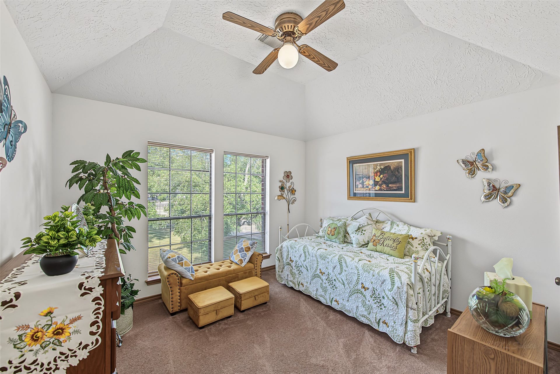 1345 Peach Ridge Road, Brookshire, TX 77423 This charming secondary bedroom features a vaulted tray ceiling with a central ceiling fan that enhances the room's sense of height and open space. Twin floor-to-ceiling windows flood the area with natural light while providing serene views of the surrounding tree-lined property.