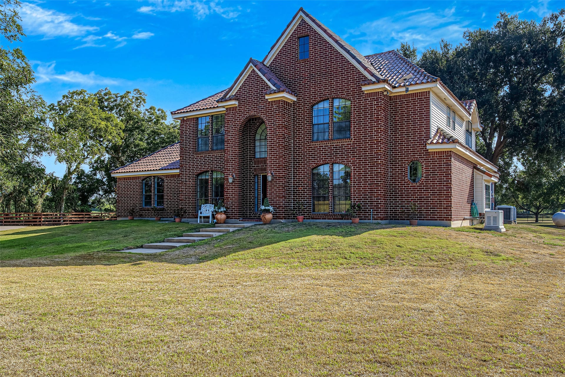 1345 Peach Ridge Road, Brookshire, TX 77423 A centered entry tower features a soaring arched transom window above the front door, flanked by large multi-pane arched windows that flood the home with natural light while providing striking curb appeal.