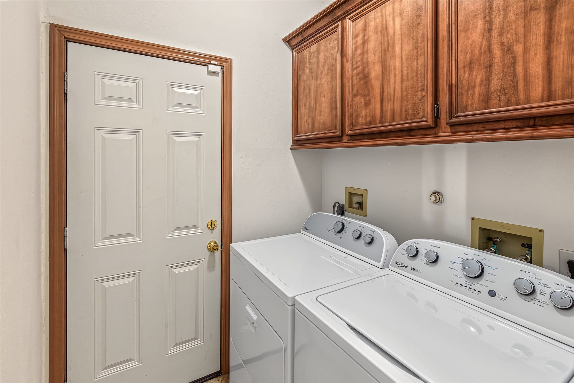 1345 Peach Ridge Road, Brookshire, TX 77423 Designed for maximum efficiency, this functional utility room features rich, custom-finished upper wood cabinetry that provides ample concealed storage for laundry supplies and everyday essentials. Situated directly alongside a white top-loading washer and dryer, the space is neatly finished with matching wood casing around the interior door, blending seamlessly with the home's cohesive millwork design.