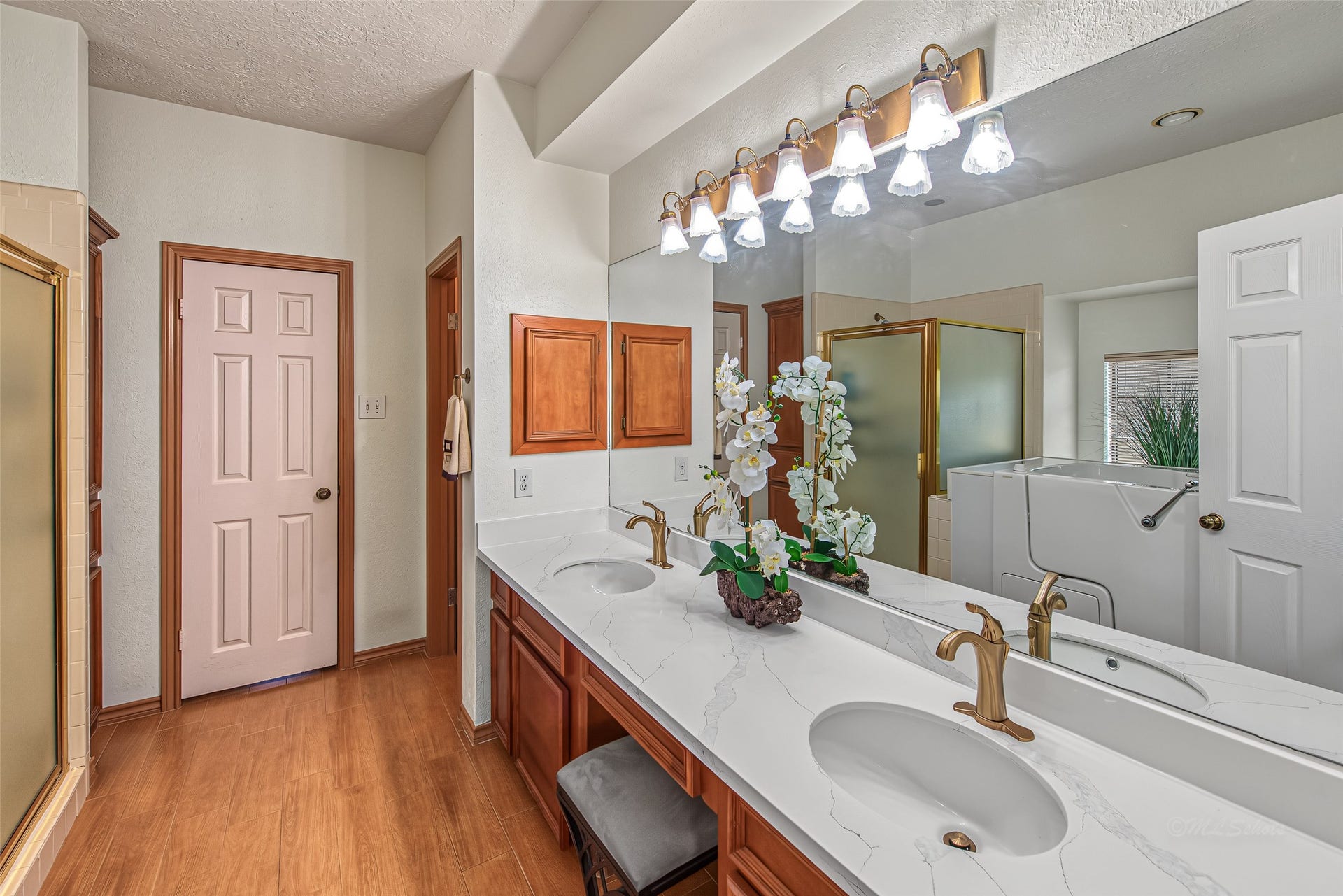 1345 Peach Ridge Road, Brookshire, TX 77423 Designed for luxurious comfort and accessibility, this primary bathroom features an expansive double vanity with marble-look quartz countertops, dual undermount sinks, warm wood cabinetry, and a dedicated sitting vanity station.