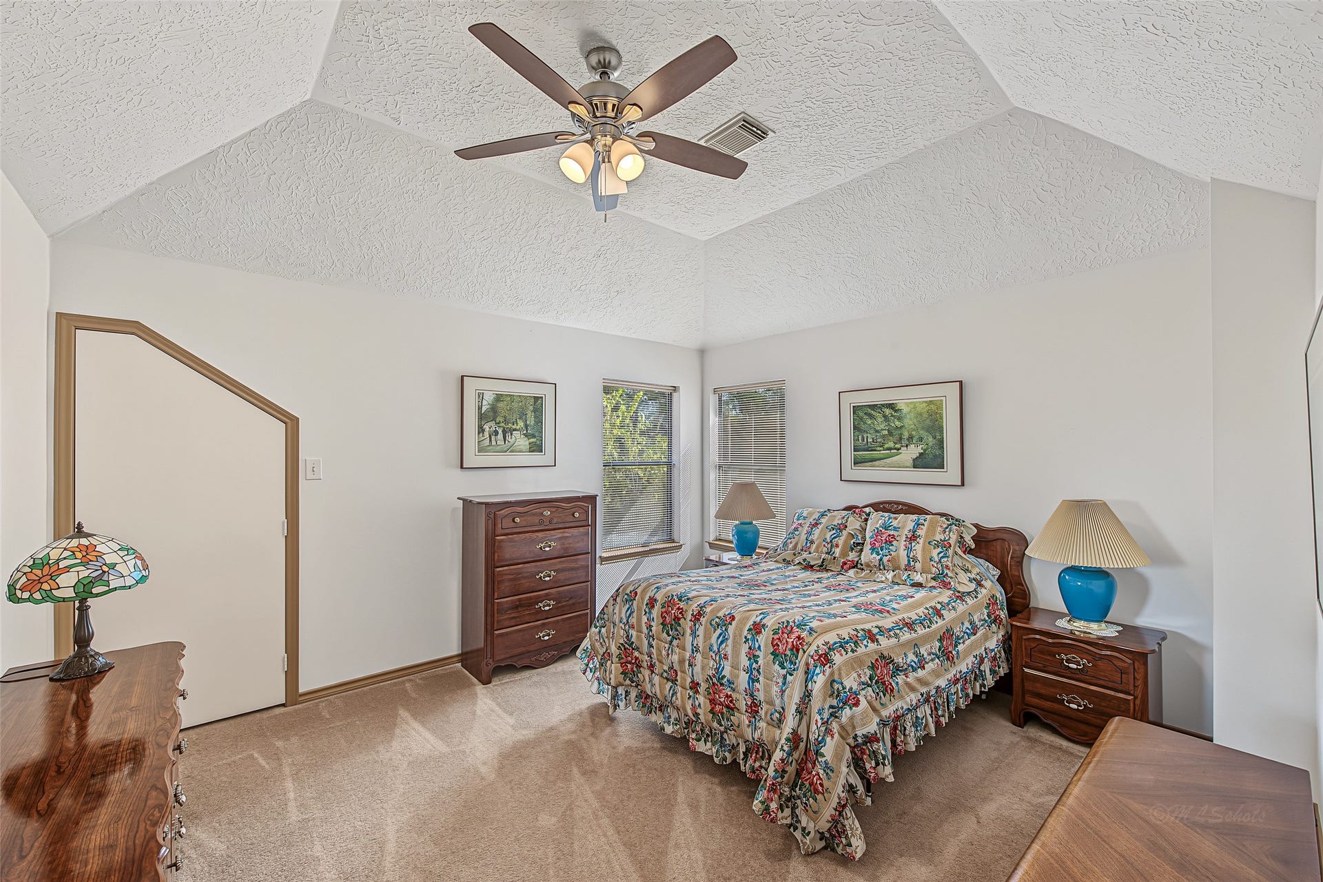 1345 Peach Ridge Road, Brookshire, TX 77423 Dramatic vaulted tray ceiling with a central ceiling fan, this spacious upper-level bedroom offers a bright and tranquil retreat. Soft, neutral carpeting underfoot and clean wall finishes create an inviting atmosphere, complemented by a unique angled door that leads to extra closet or under-roof storage.