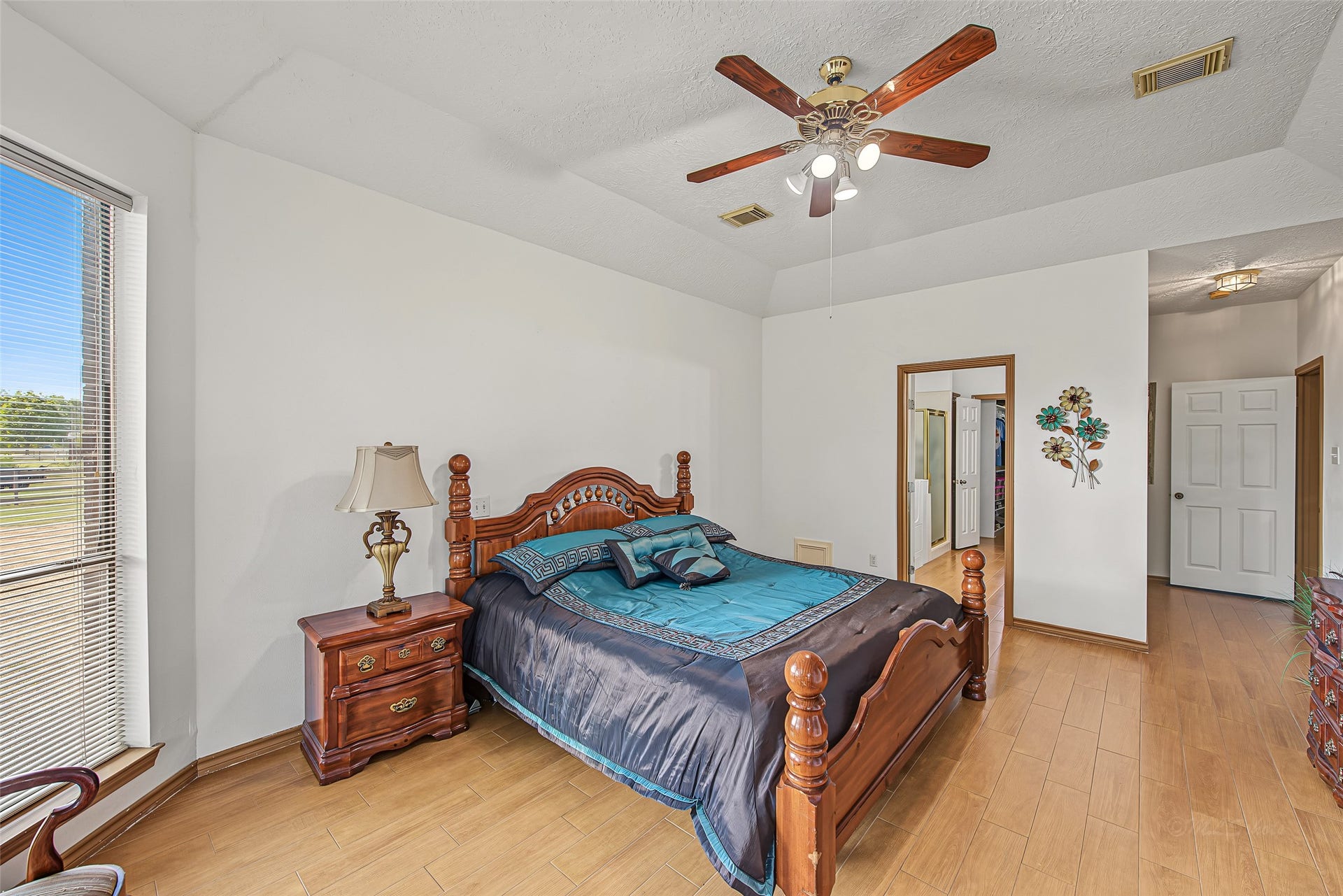 1345 Peach Ridge Road, Brookshire, TX 77423 This primary retreat offers an airy sanctuary defined by impressive tray ceilings with a central ceiling fan and warm, light-toned wood flooring.