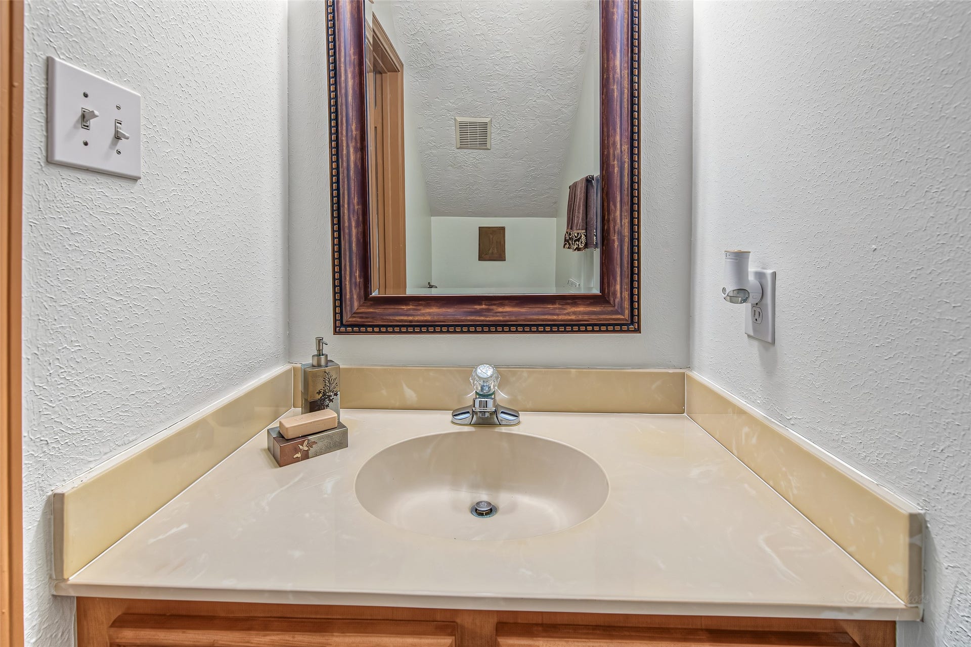 1345 Peach Ridge Road, Brookshire, TX 77423 Conveniently located for guests, this elegant powder room features a smooth cultured marble vanity top with an integrated sink and a matching full-length backsplash. Set against clean, light walls, the space is highlighted by a rich, dark-stained framed mirror with decorative bead molding that adds a touch of classic warmth.