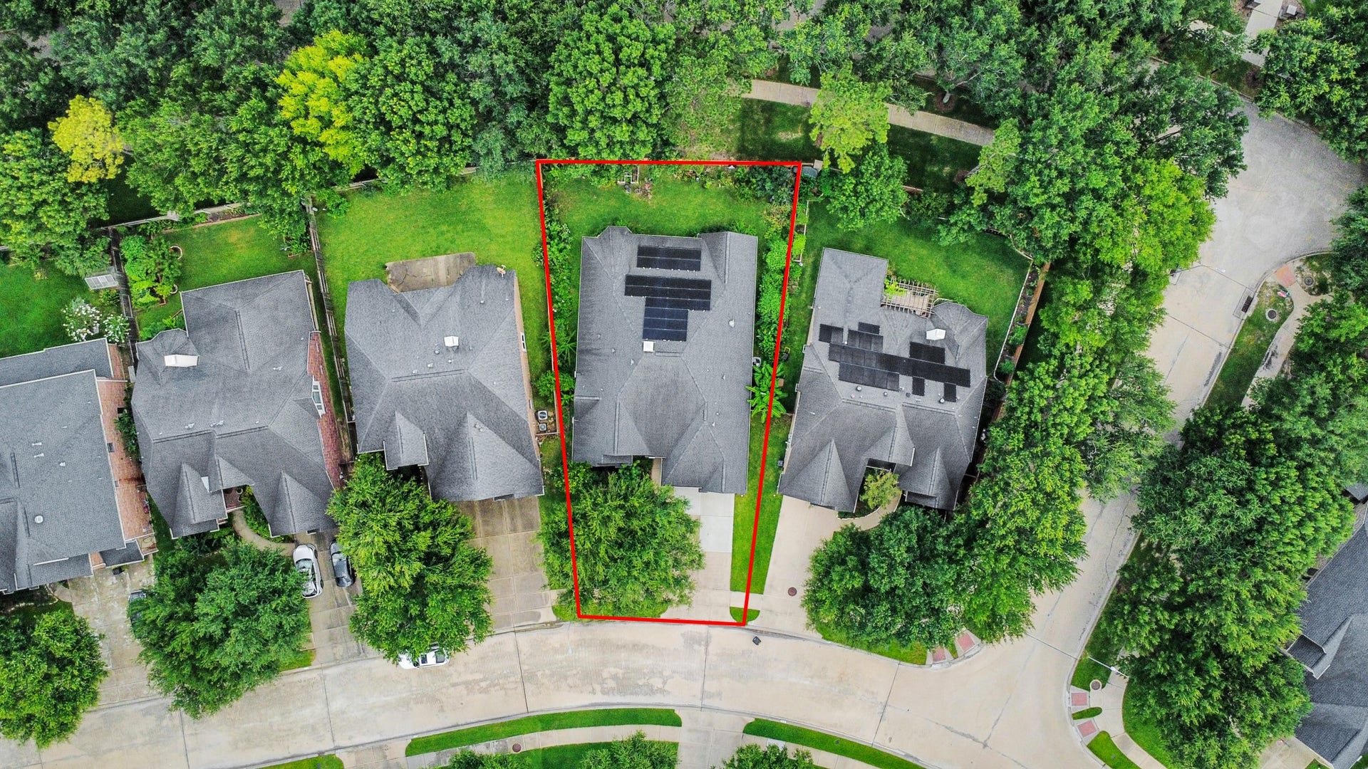 21123 Dover Park Lane, Katy, TX 77450 This aerial view shows a house with a spacious backyard outlined in red, nestled in a leafy neighborhood. The roof has solar panels, and the property is surrounded by mature trees, offering privacy and greenery.