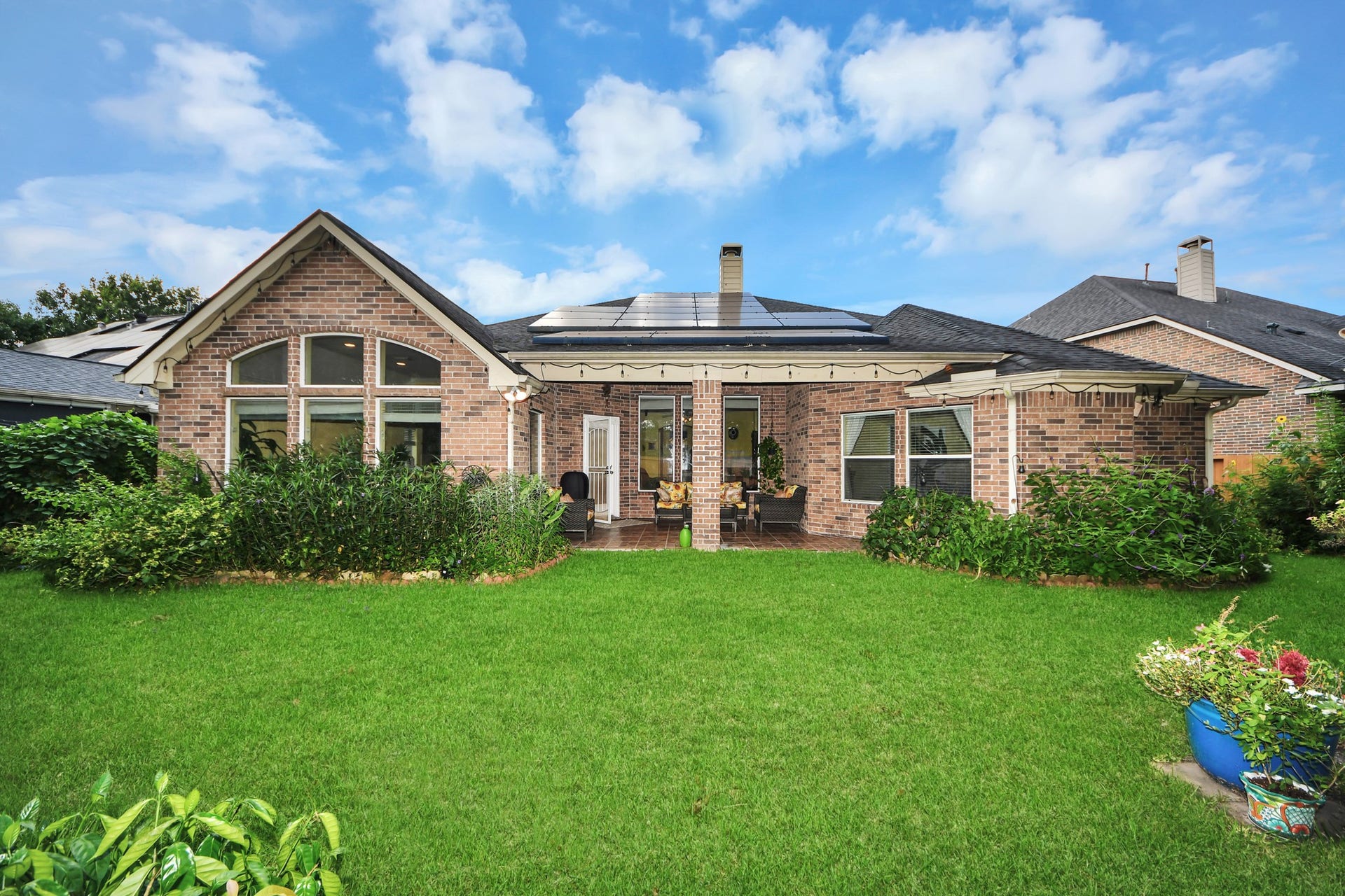 21123 Dover Park Lane, Katy, TX 77450 This photo showcases a charming brick home with solar panels on the roof. It features a well-maintained backyard with lush greenery and a cozy patio area, perfect for outdoor relaxation.