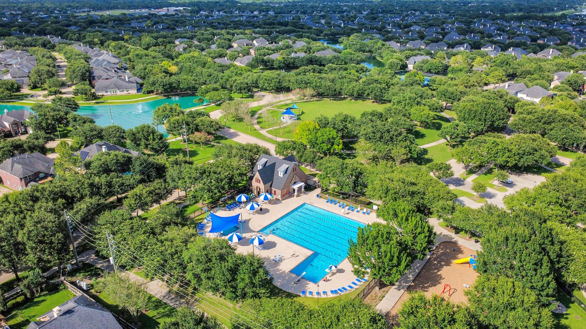 21123 Dover Park Lane, Katy, TX 77450 This aerial photo showcases a vibrant neighborhood with lush greenery, featuring a large community pool, playground, and walking paths. Residences are nestled among trees, offering a serene suburban setting.
