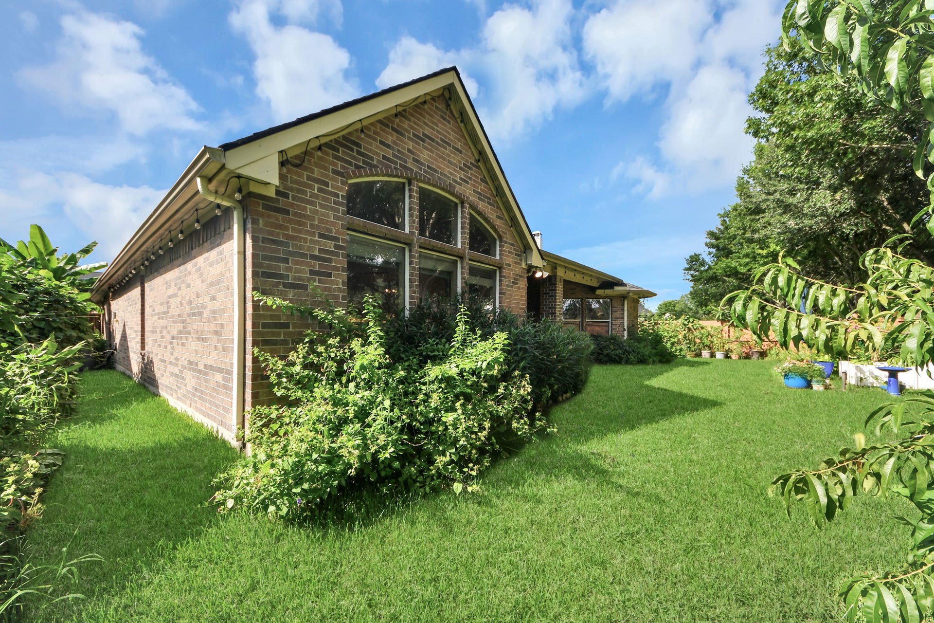 21123 Dover Park Lane, Katy, TX 77450 This photo showcases a charming brick home with a lush, green backyard. The house features large windows and a well-maintained lawn surrounded by mature trees and shrubs, offering a serene and private outdoor space.