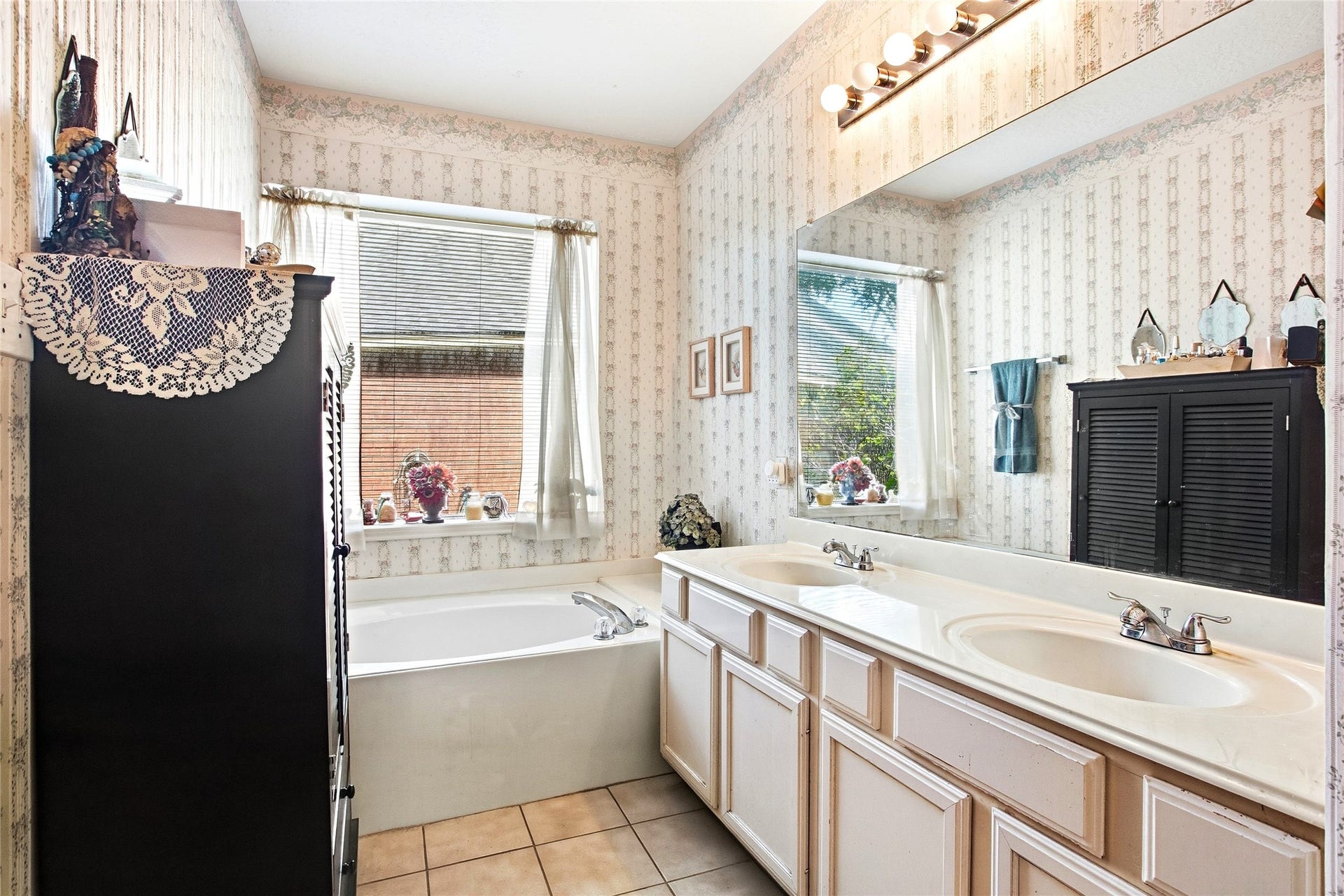 Primary bath with a soaking tub beneath a window, double-sink vanity, and tile flooring.