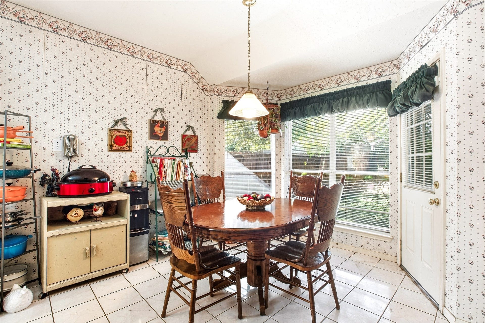 Breakfast area off the kitchen with tile flooring, a pendant light, large windows overlooking the backyard, and a door to the rear yard.