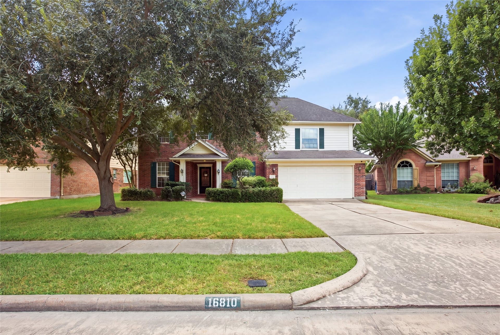 Curb view framed by a large mature shade tree, with a curved front walk and wide driveway.