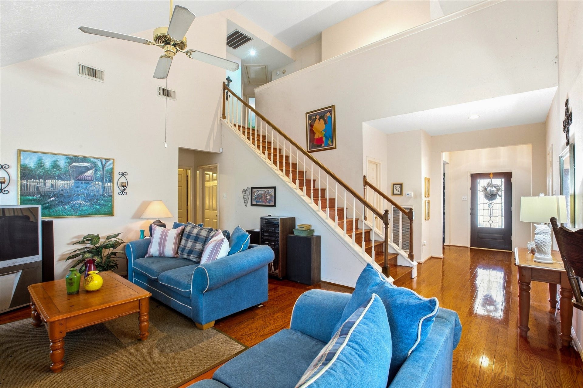 Family room view toward the staircase and front entry, with a vaulted ceiling and engineered wood floors.