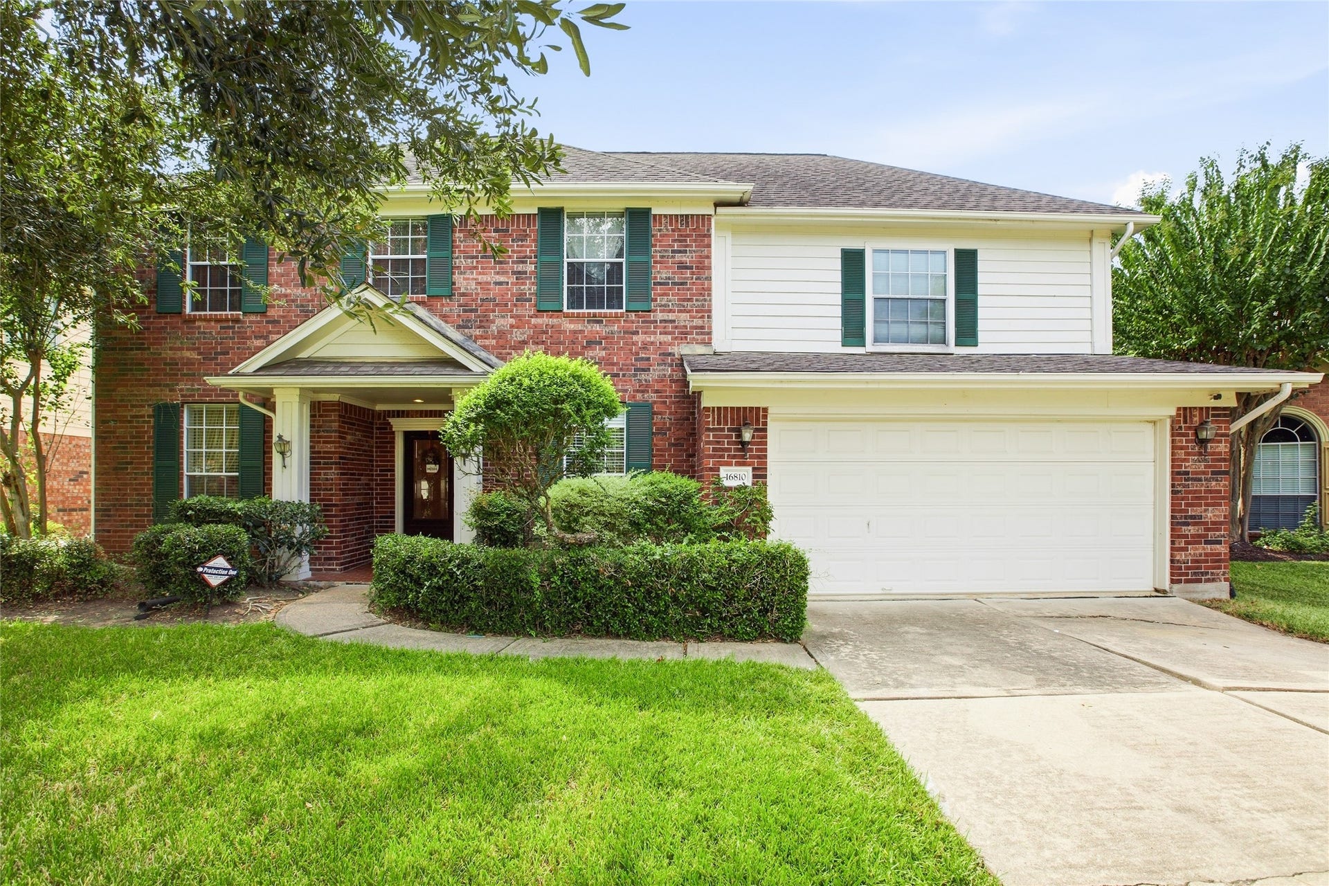 Front exterior showing the covered entry, sculpted hedges, and attached two-car garage with coach lights.