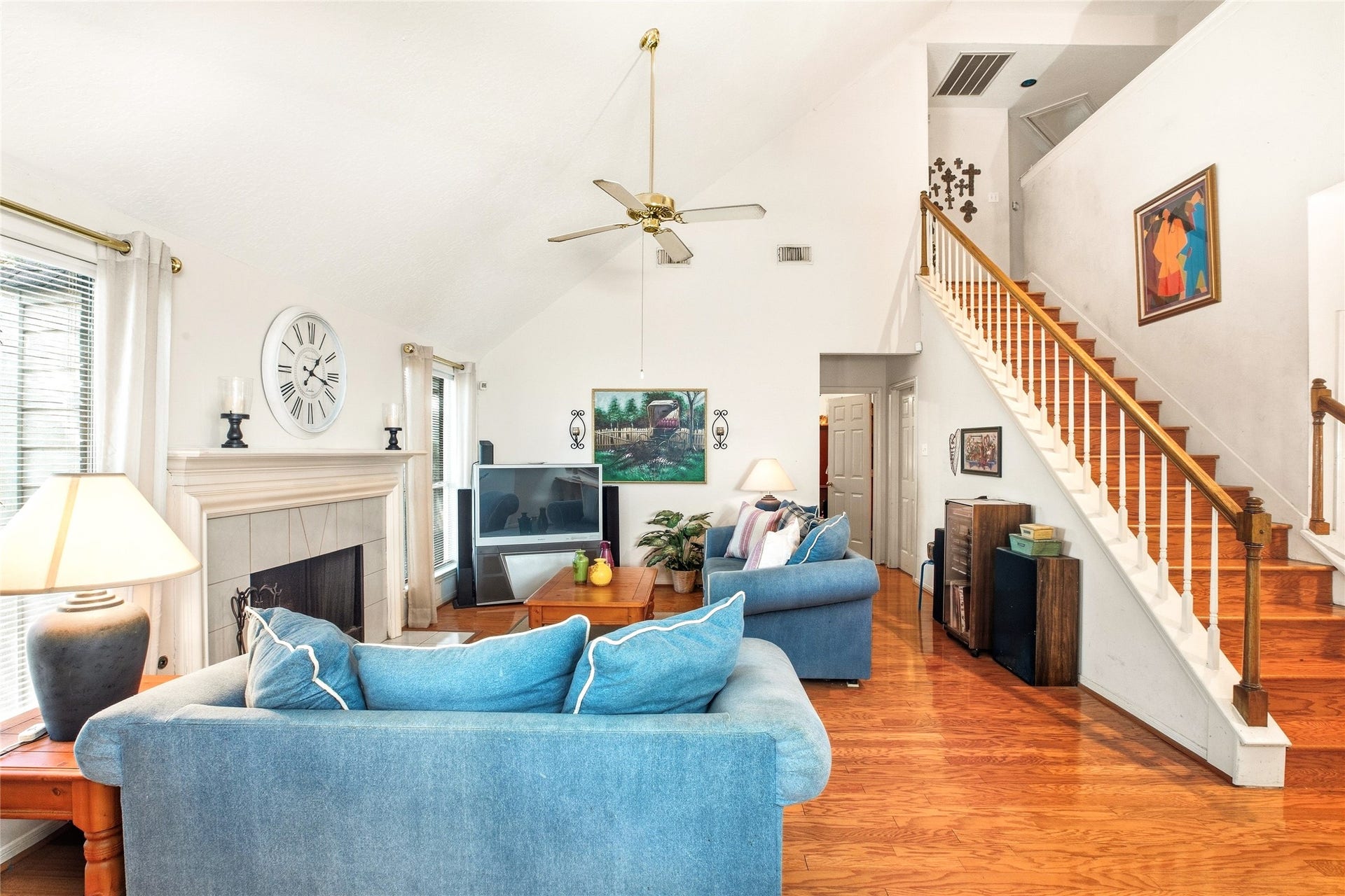 Family room with a soaring vaulted ceiling, tile-surround fireplace, ceiling fan, and engineered wood floors, open to the staircase.