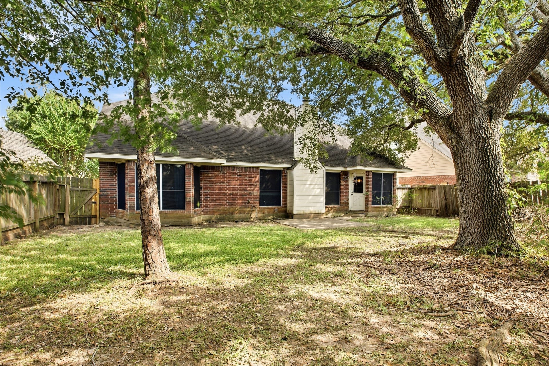 Large backyard shaded by mature trees and enclosed by a wood privacy fence, with a view of the rear of the home.