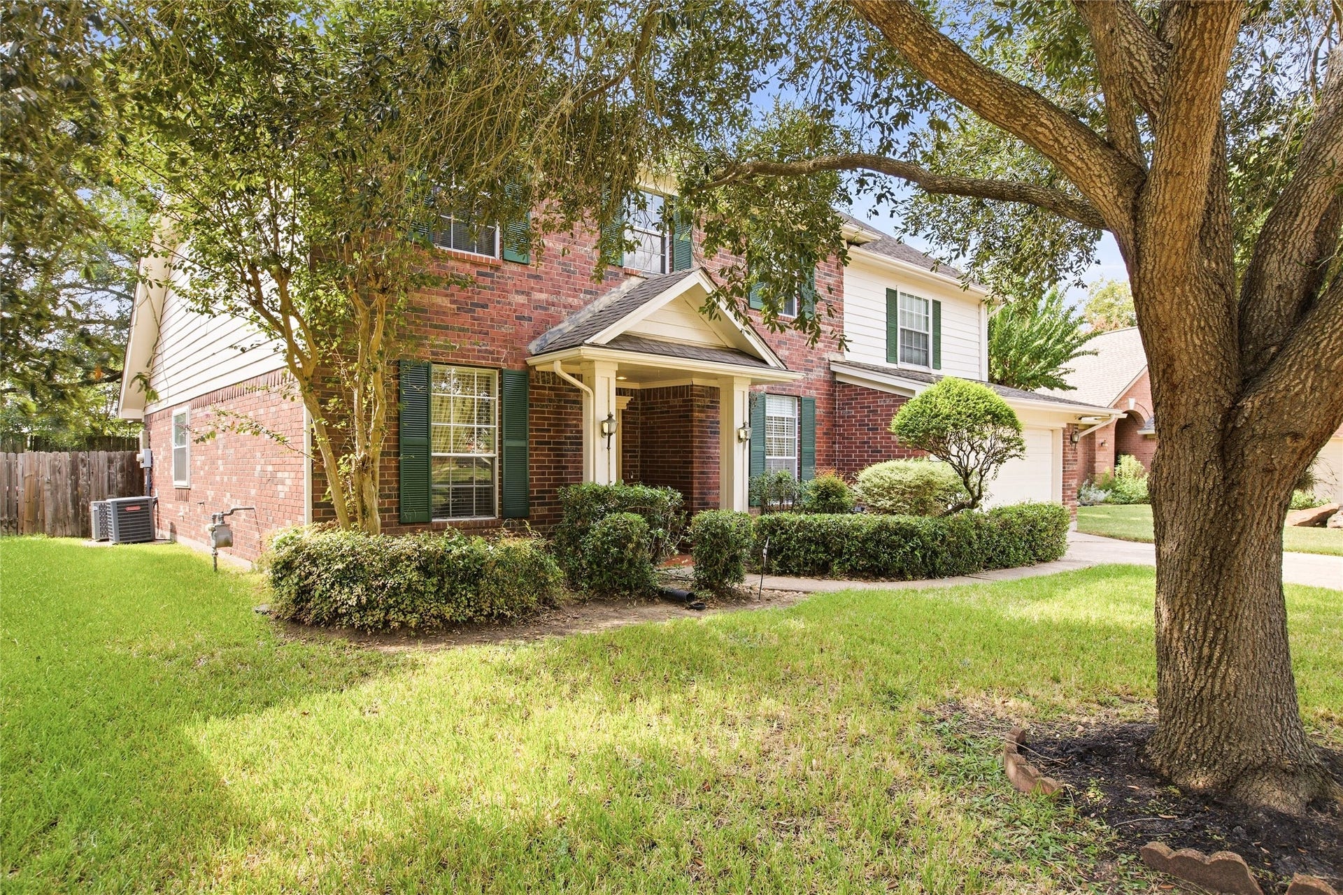Front yard with a mature shade tree, established landscape beds, and a full green lawn.