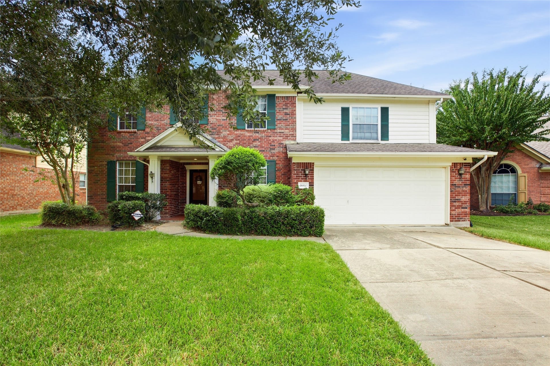Front elevation with brick and siding exterior, covered entry, shaped shrubs, and a wide concrete driveway leading to the two-car garage.