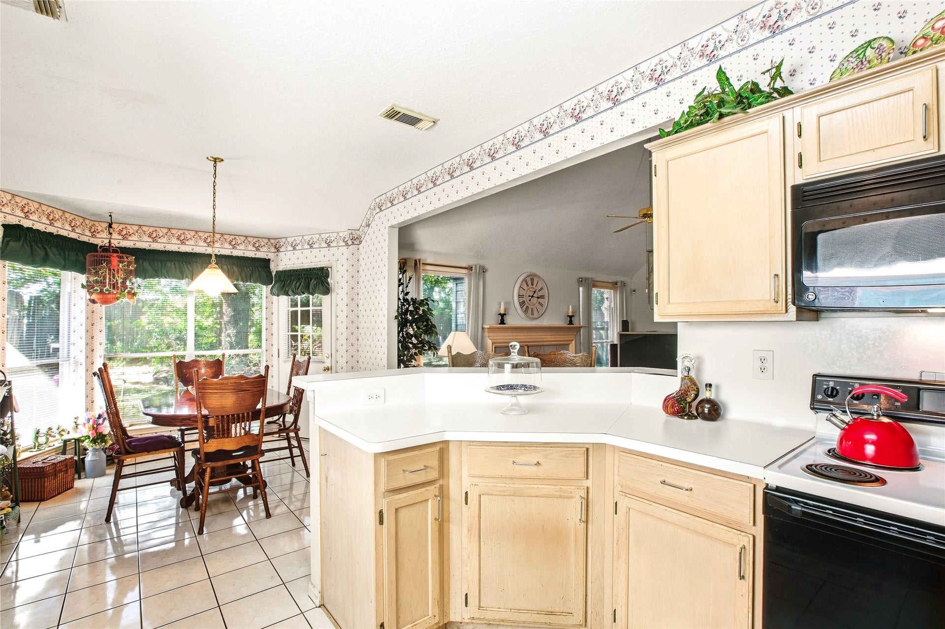 Kitchen peninsula with white countertops and light wood cabinetry, overlooking the breakfast area and its bay window, with a built-in microwave above the range.