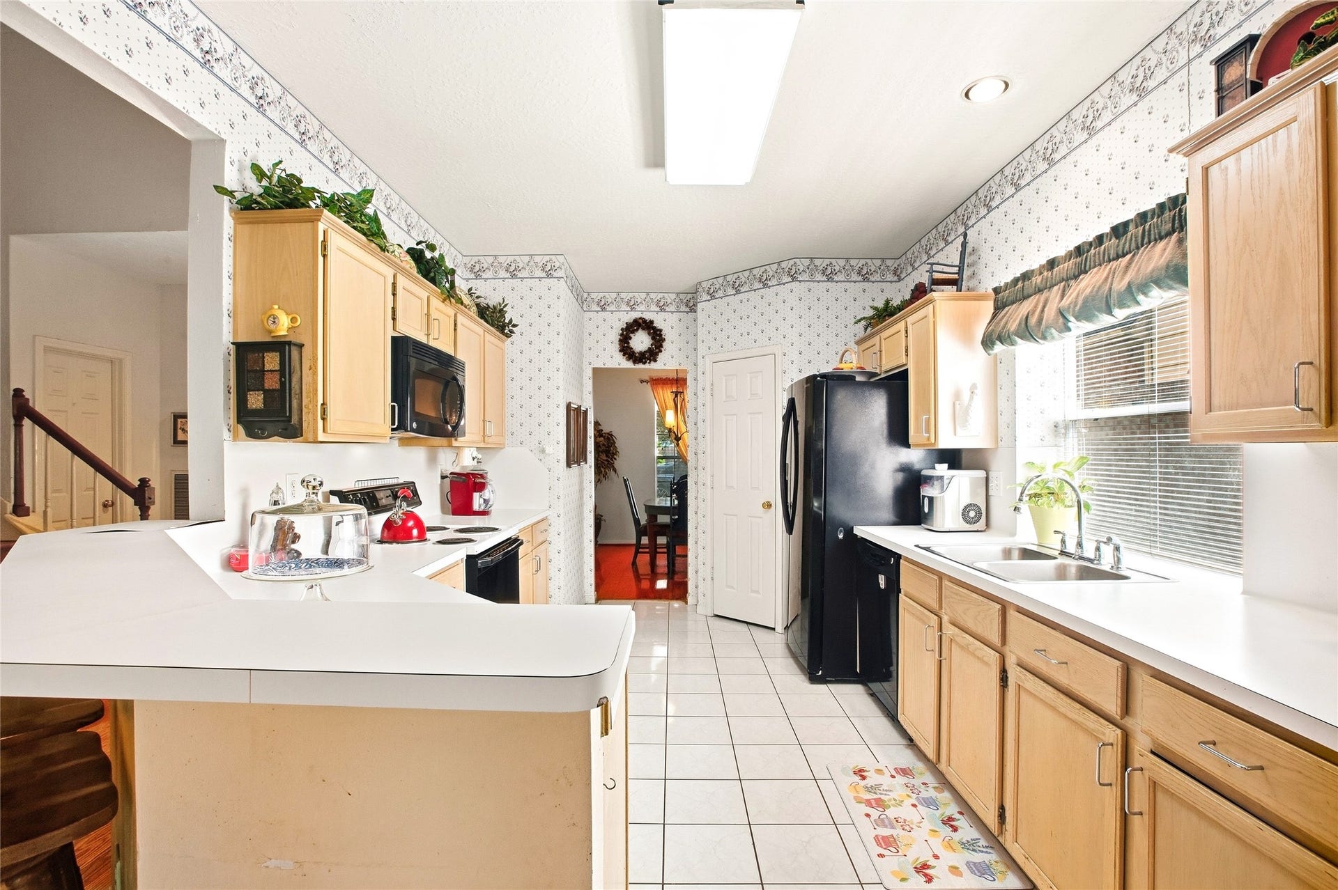 Kitchen with generous counter space along two walls, light wood cabinetry, a window over the sink, and a peninsula that opens to the family room.