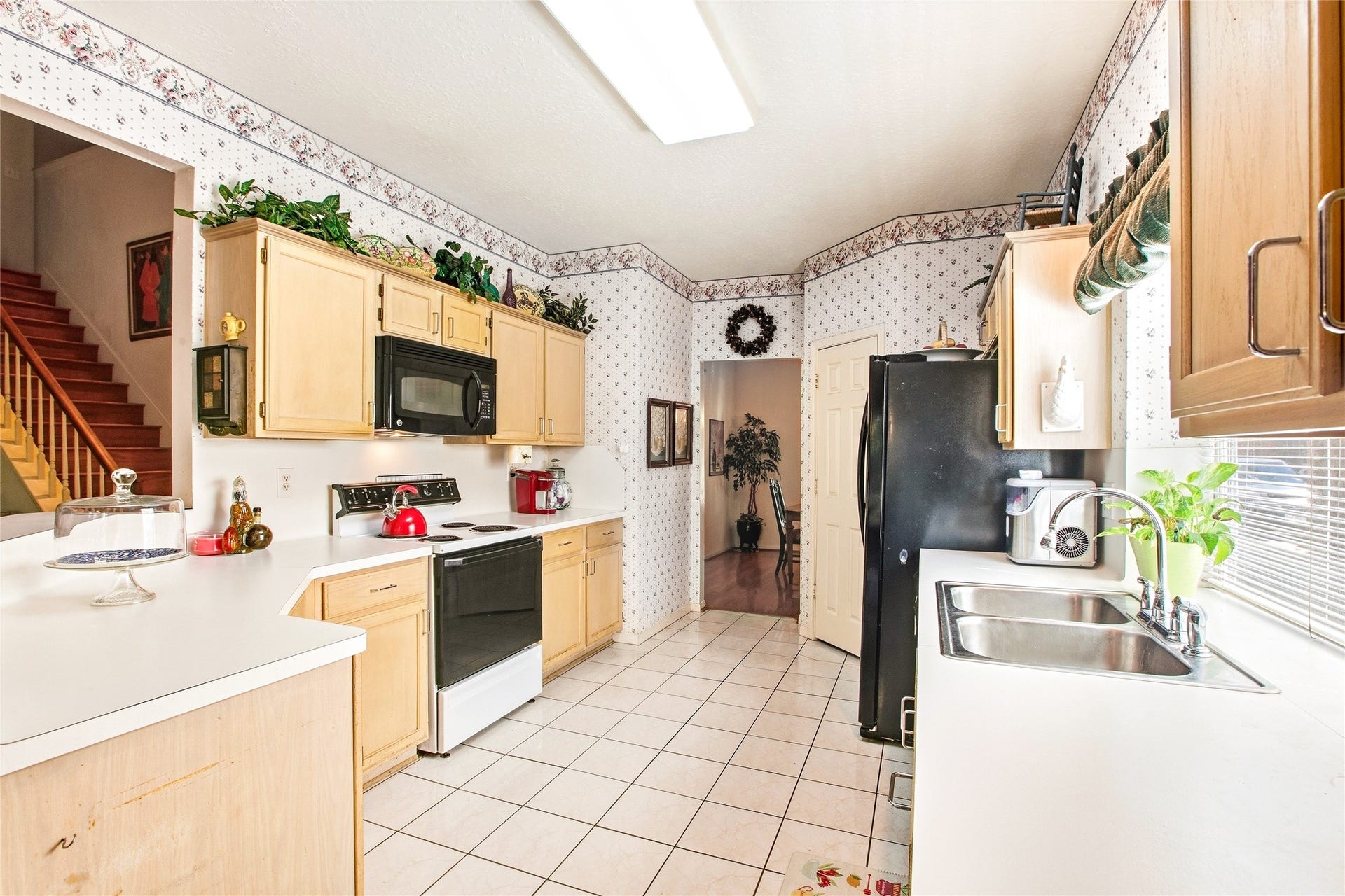 Galley kitchen view with an electric range, built-in microwave, and pantry door, with light wood cabinetry and tile flooring flowing toward the staircase.