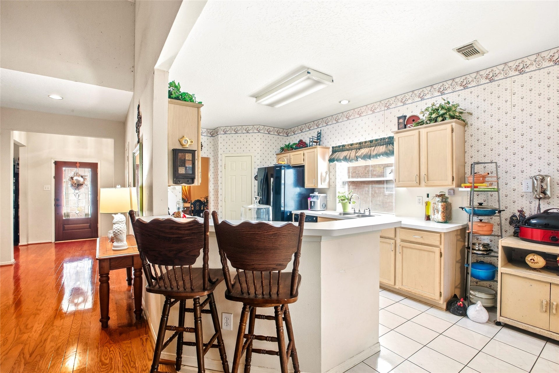 Kitchen peninsula with breakfast bar seating, where tile flooring meets the wood floors of the entry, with sightlines to the front door.