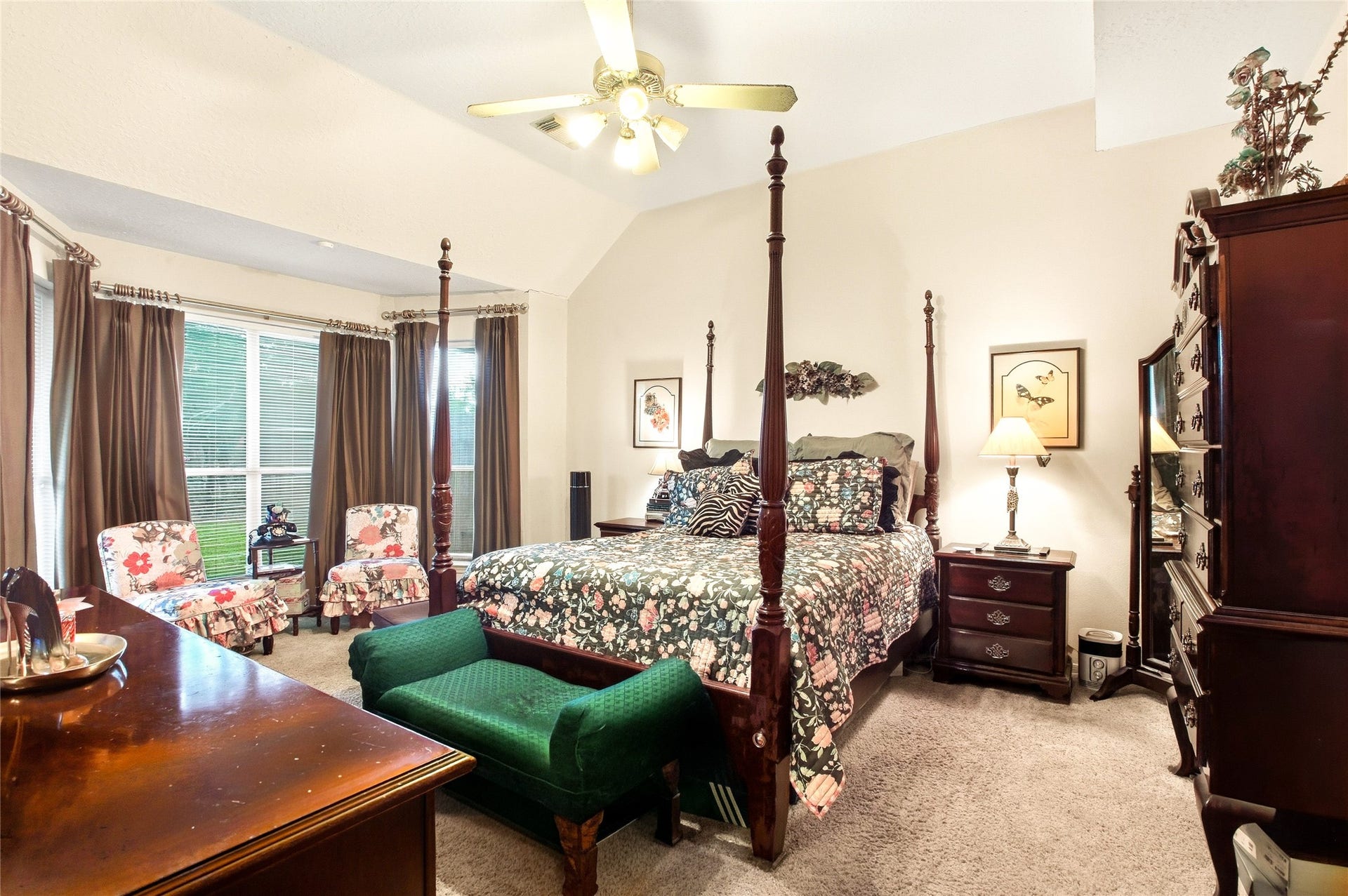 First-floor primary bedroom with a vaulted ceiling, ceiling fan, carpet, and a bank of windows with room for a sitting area.