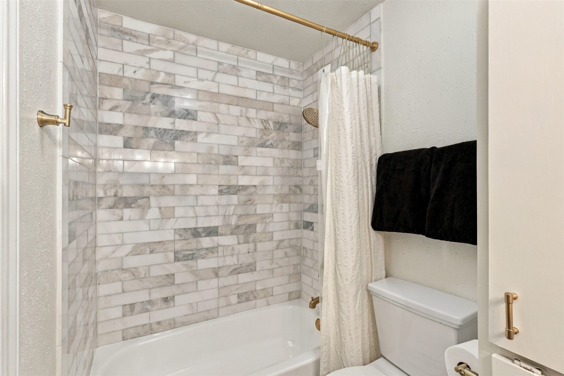 1201 Mcduffie Street, #212, Houston, TX 77019 Elegant bathroom featuring a luxurious marble-tiled shower, complemented by a classic white bathtub and gold fixtures.