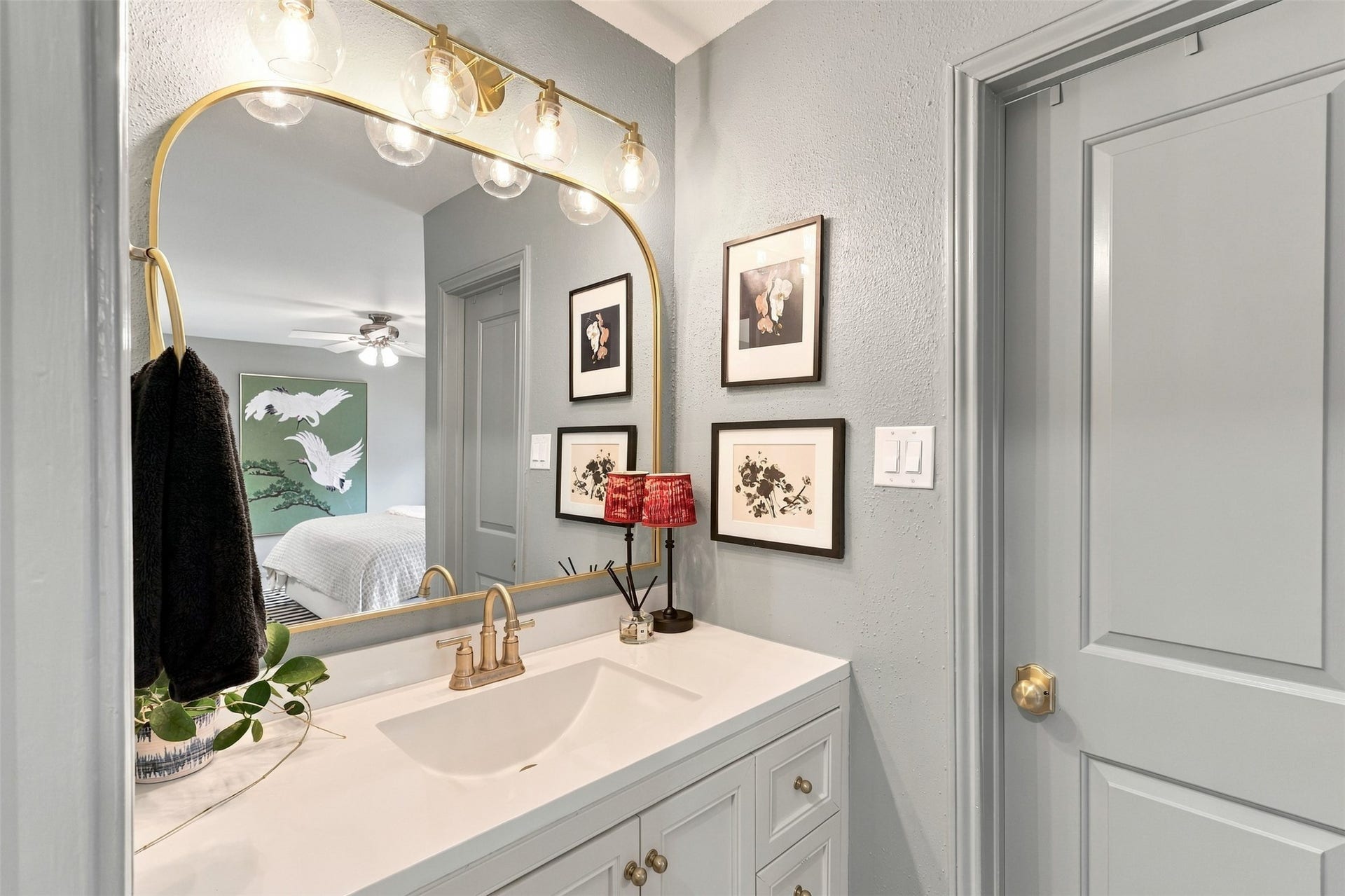 1201 Mcduffie Street, #212, Houston, TX 77019 Stylish bathroom features a sleek vanity with a gold-framed mirror, elegant lighting, and tasteful artwork, providing a modern and inviting atmosphere.