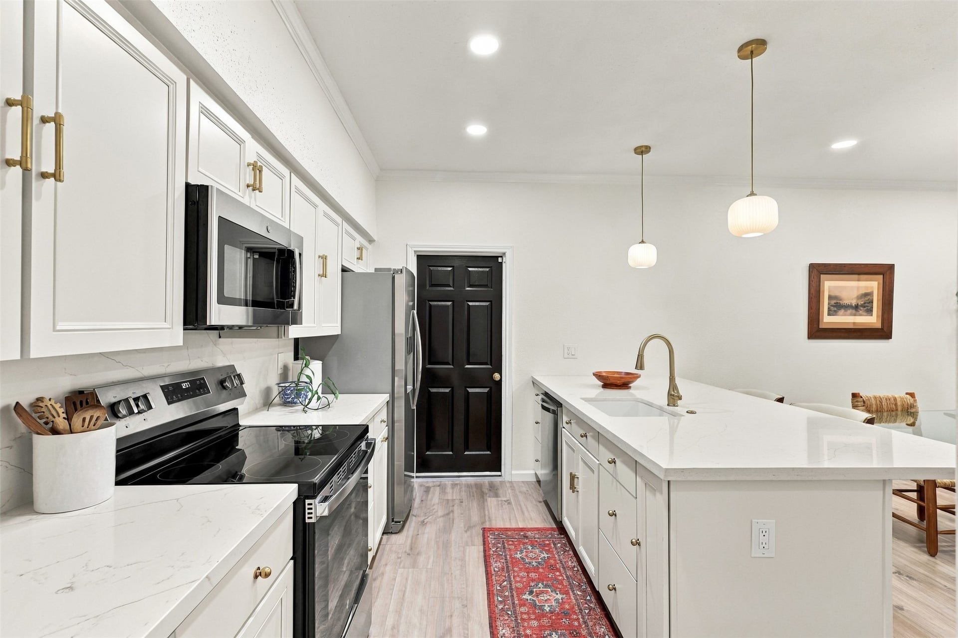 1201 Mcduffie Street, #212, Houston, TX 77019 Modern kitchen with sleek white cabinetry, stainless steel appliances, and a spacious island featuring elegant pendant lighting.