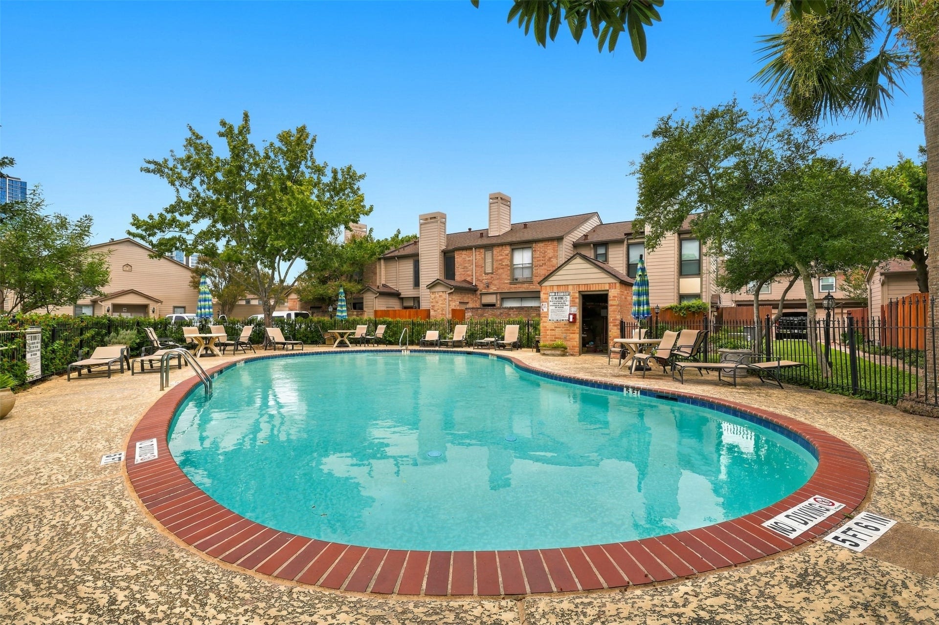 1201 Mcduffie Street, #212, Houston, TX 77019 Relax by the sparkling community pool, surrounded by lush greenery and comfortable lounge seating, perfect for enjoying sunny days.