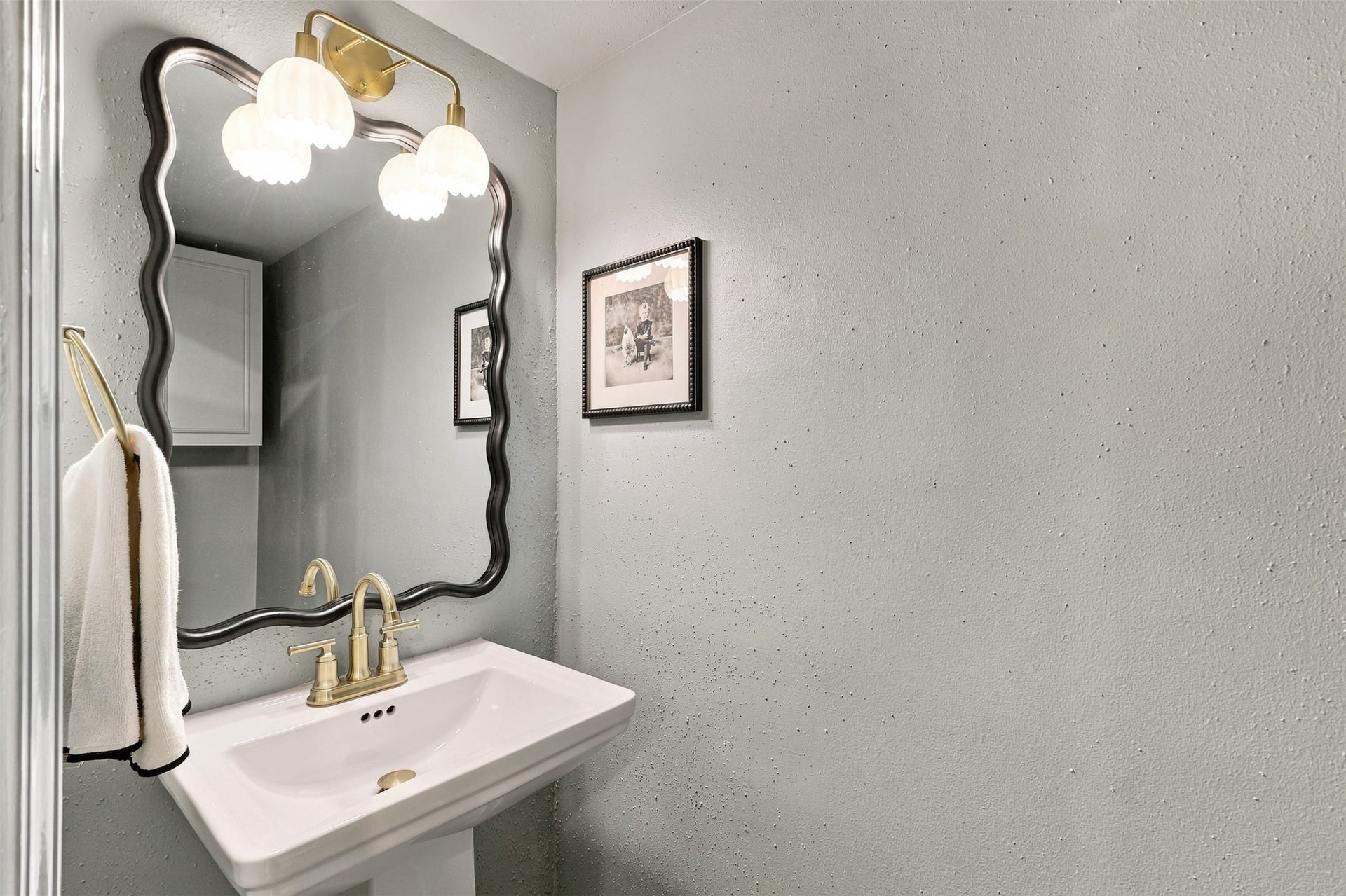 1201 Mcduffie Street, #212, Houston, TX 77019 Charming powder room featuring a sleek pedestal sink, elegant gold fixtures, and a decorative mirror, complemented by soft lighting and subtle wall art.