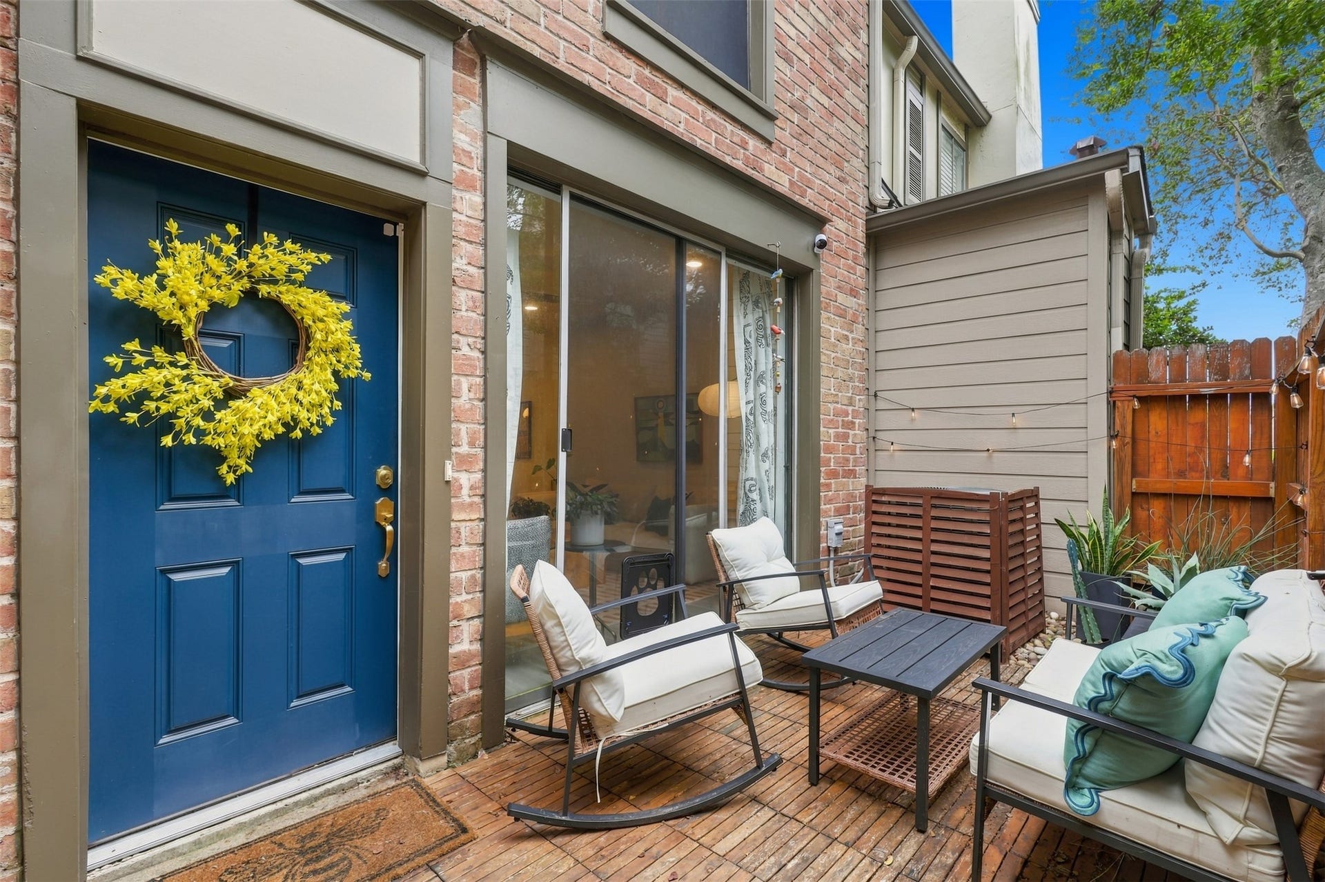 1201 Mcduffie Street, #212, Houston, TX 77019 Charming patio features cozy seating, a vibrant blue door with a cheerful wreath, and a warm brick exterior, perfect for relaxing or entertaining.