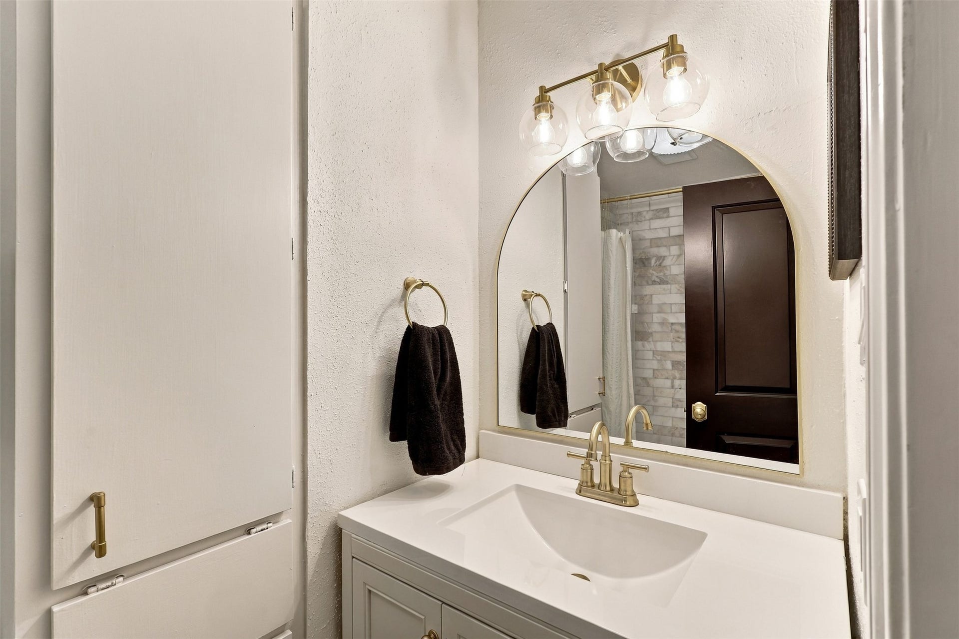 1201 Mcduffie Street, #212, Houston, TX 77019 Elegant bathroom featuring a modern vanity with a sleek countertop, complemented by a stylish arched mirror and chic lighting fixtures.