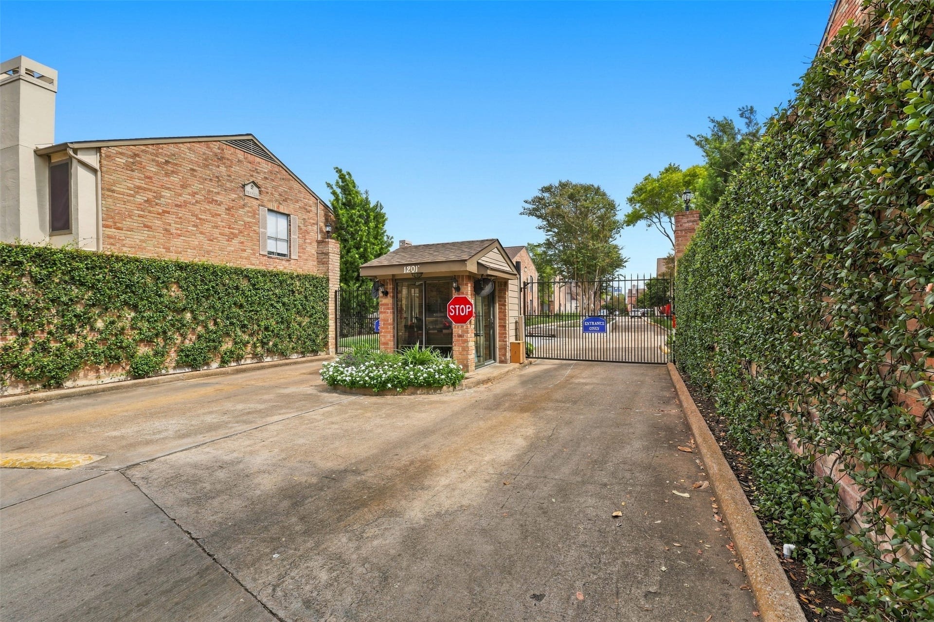 1201 Mcduffie Street, #212, Houston, TX 77019 Gated community entrance featuring lush greenery and a welcoming security booth, providing privacy and peace of mind.