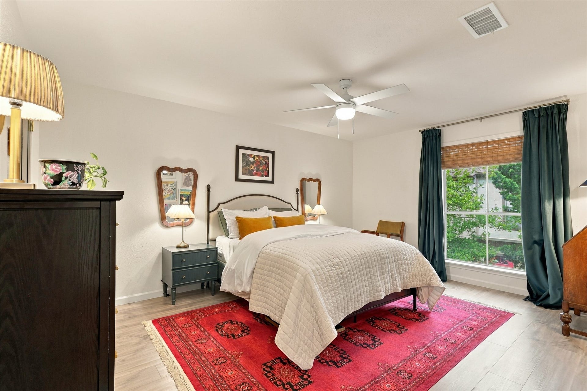 1201 Mcduffie Street, #212, Houston, TX 77019 Spacious and bright bedroom featuring a cozy bed with elegant bedding, large window with rich drapes, and a vibrant red area rug adding warmth and style.