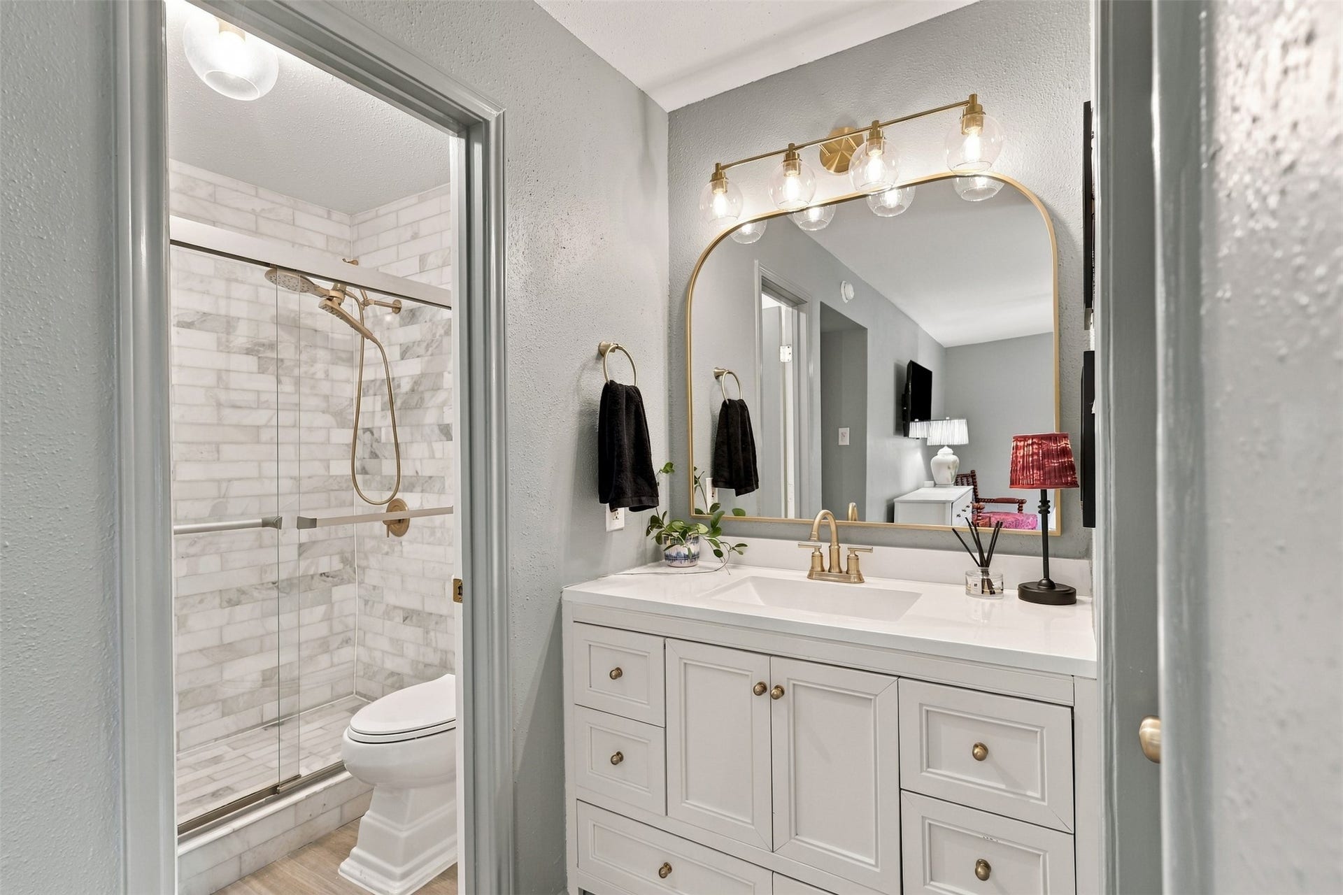 1201 Mcduffie Street, #212, Houston, TX 77019 Elegant bathroom featuring a stylish vanity with a gold-framed mirror, modern light fixtures, and a glass-enclosed marble shower.
