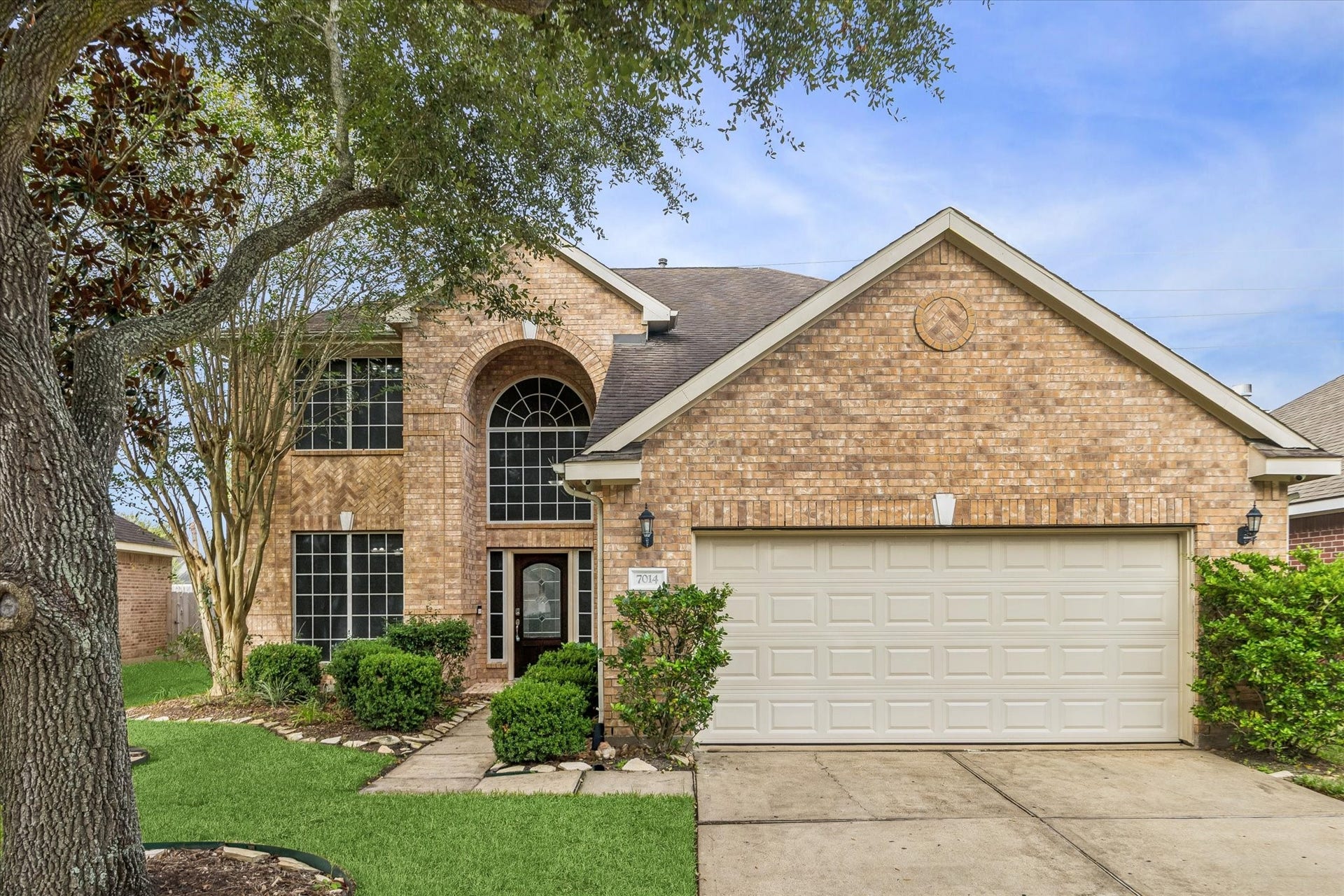 7014 Baristone Lane, Richmond, TX 77407 Charming two-story brick home with mature trees, an elegant arched entry, and two-car garage.
