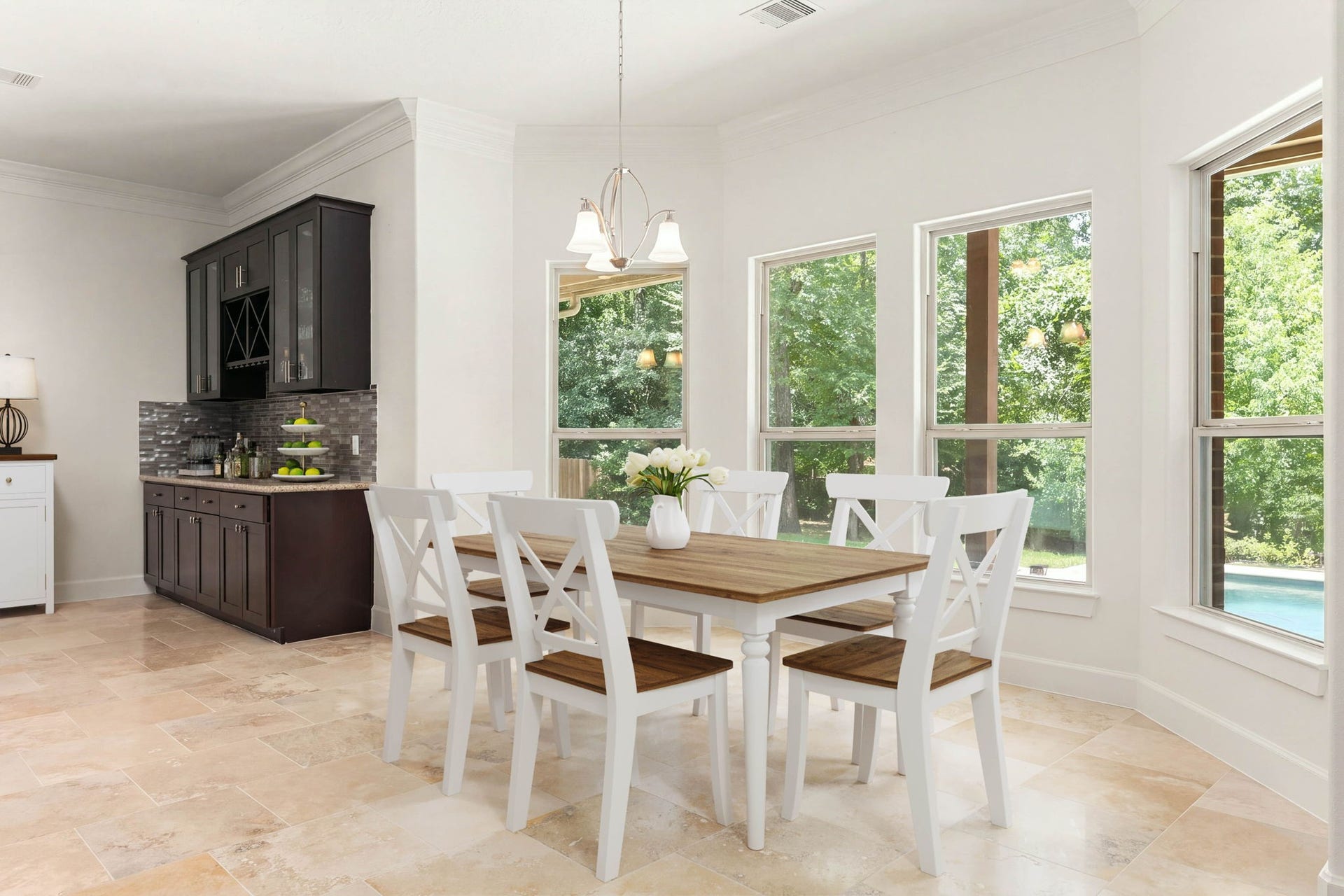 Sunlit and spacious, this beautiful dining area features walls of windows framing serene outdoor views and premium travertine tile flooring. The custom built-in buffet provides the ultimate setup for a coffee station, wine bar, or holiday serving space.