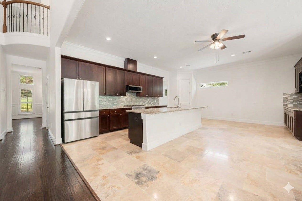 This spacious, open-concept kitchen and dining area features rich dark cabinetry, sleek stainless steel appliances, and a beautiful tile backsplash. A large center island provides plenty of prep space and looks out over the expansive tile floors, creating a perfect setup for entertaining guests.