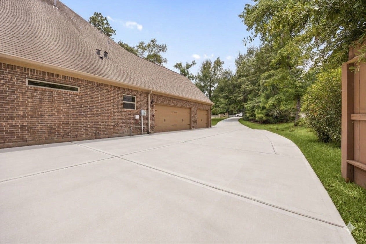 An expansive concrete driveway leads to a spacious three-car garage, highlighting the home's ample parking space.