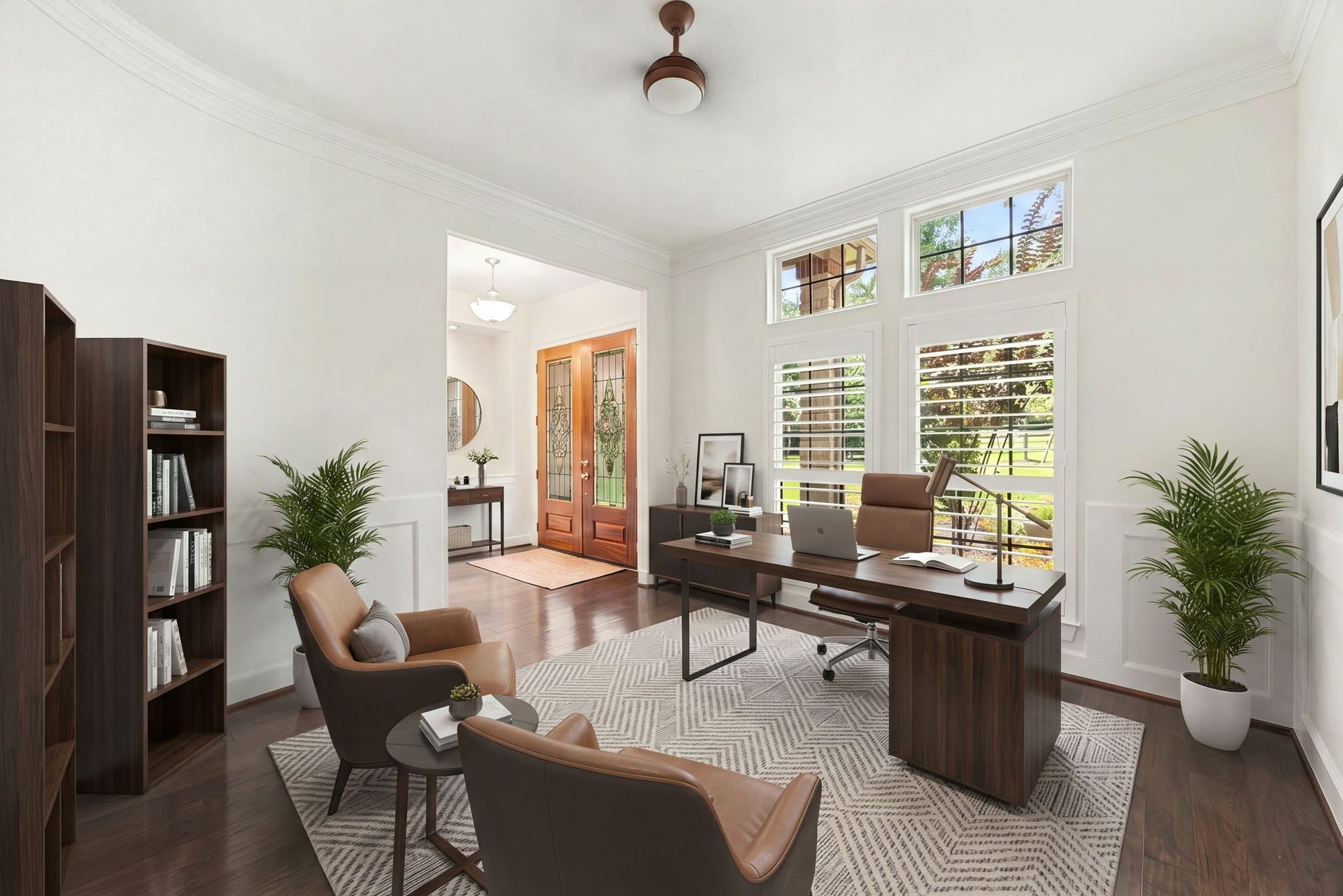 This flexible home office space features rich dark hardwood floors, crisp white walls with elegant wainscoting trim, and a soaring ceiling equipped with a modern ceiling fan. Expansive windows fitted with classic plantation shutters flood the room with brilliant natural light while offering peaceful views of the front yard. *Virtually Staged