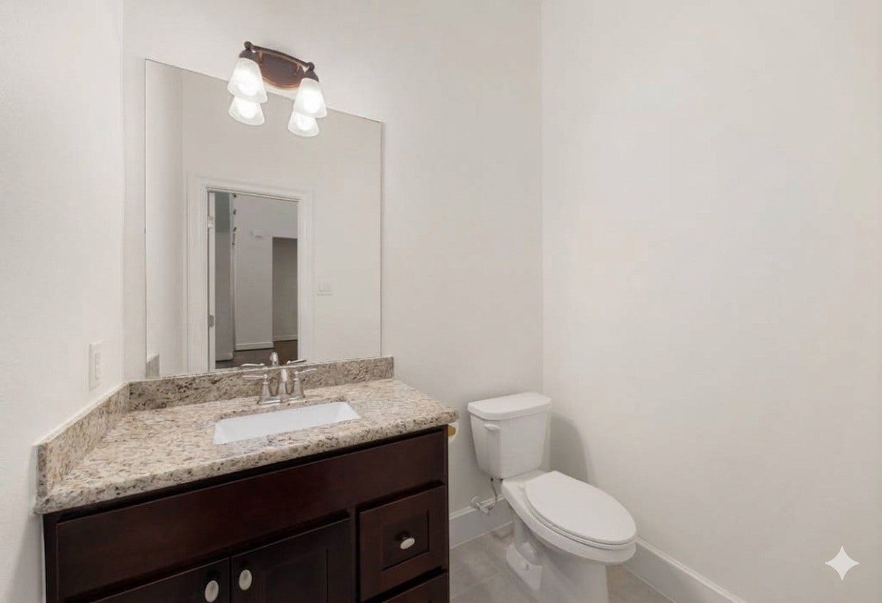 This crisp and neutral powder room features a dark wood vanity topped with beautiful granite counters. A large frameless mirror and an updated light fixture help keep the space feeling bright, open, and inviting for your guests.