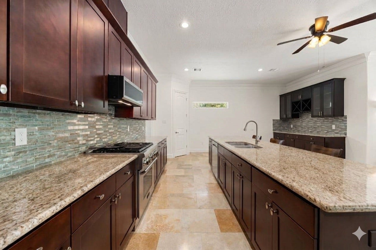 This chef-inspired kitchen showcases premium granite countertops, rich wood cabinetry, and a beautiful shimmering glass tile backsplash. The massive central island offers a deep double sink and expansive meal prep space, making it perfect for both daily cooking and lively entertaining.