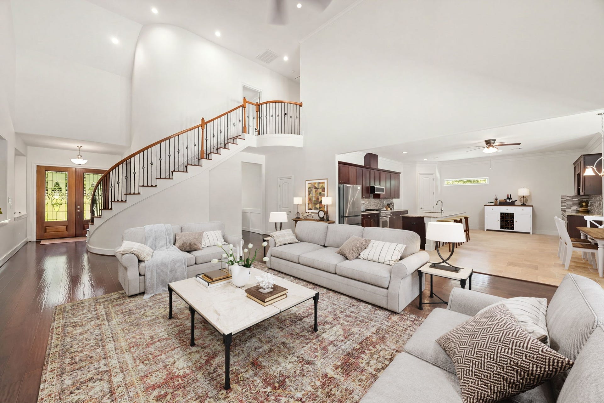 This wide-angle perspective showcases the home's spectacular open-concept design, perfectly blending the living, dining, and cooking areas. The grand family room flows effortlessly into the modern kitchen, while the dramatic curved staircase serves as an elegant backdrop to the entire main level. *Virtually Staged