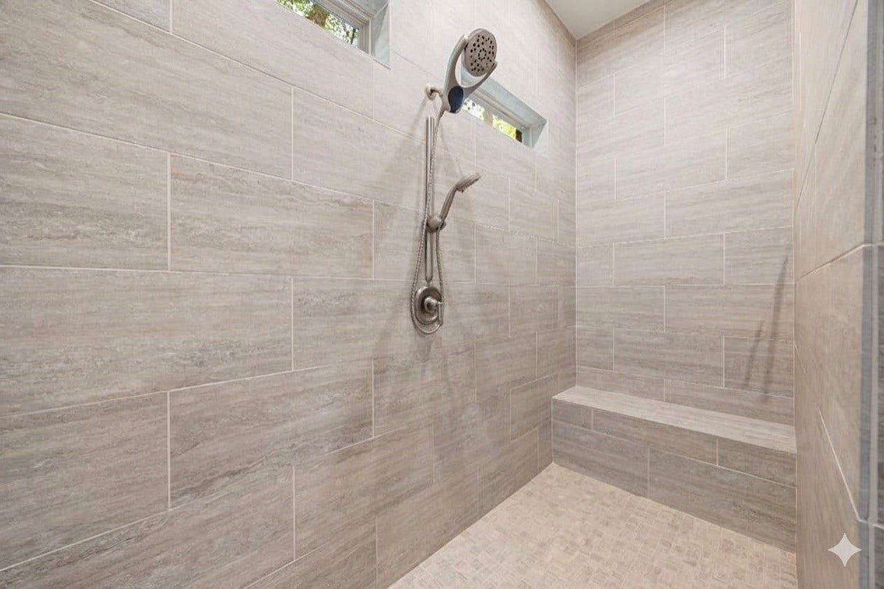 This luxurious walk-in shower features a neutral tile surround, a built-in bench seat, and a mosaic tile floor. The space is complete with high window cutouts for natural light and a dual shower head system that offers both a traditional wall mount and a flexible handheld sprayer.