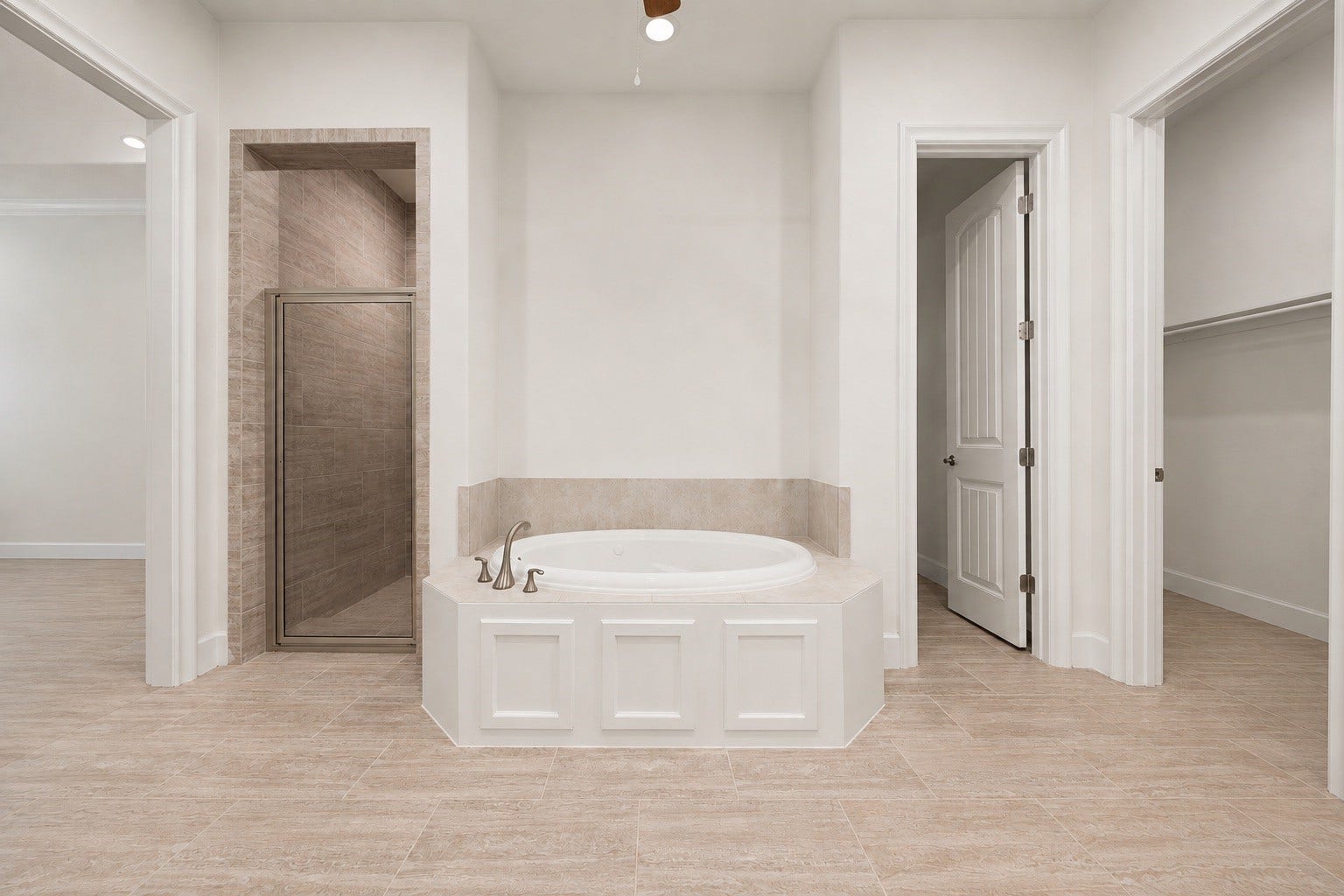 This primary bathroom view highlights a relaxing central soaking tub nestled between a separate glass-enclosed walk-in shower and a spacious walk-in closet. The room features gorgeous floors, classic wainscoting tub trim, and a bright, neutral color palette that feels like a private spa.