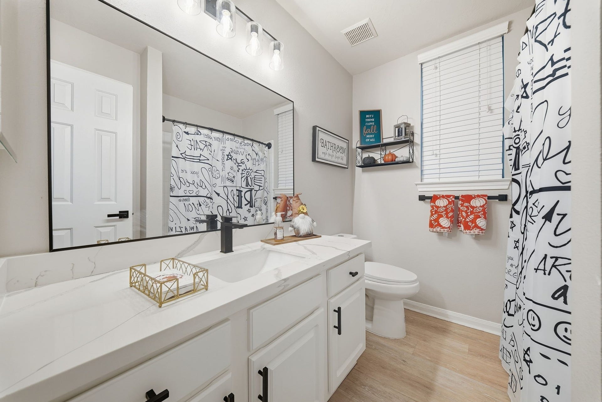 402 Prattwood Court, League City, TX 77573 Updated bathroom with quartz vanity, large framed mirror, black fixtures, and glass-enclosed shower with patterned curtain.