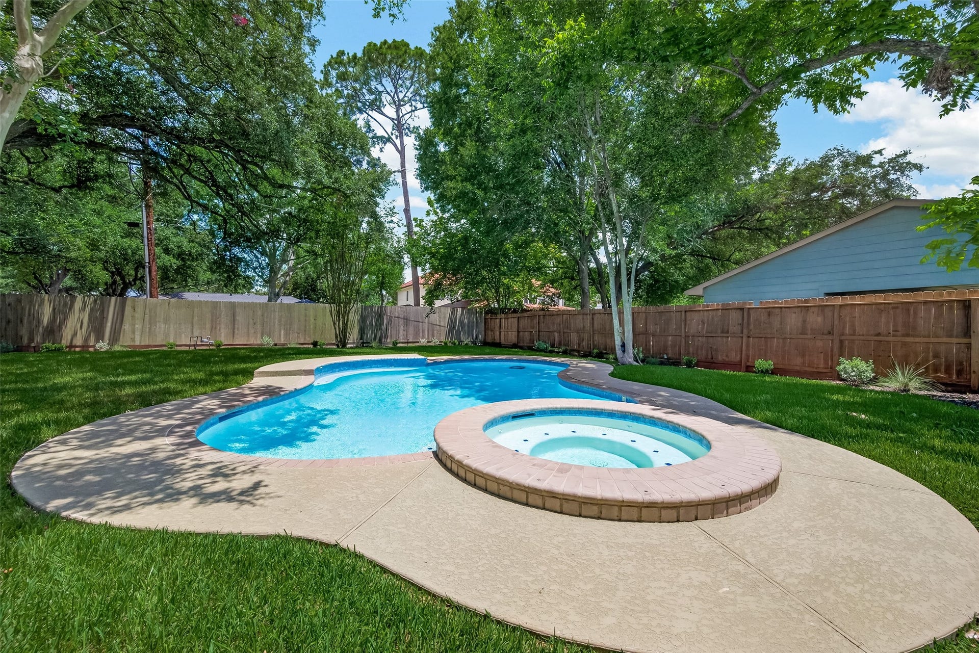 5422 Valerie Street, Bellaire, TX 77401 This backyard features a beautifully landscaped area with a sparkling pool and attached spa, surrounded by lush grass and mature trees, offering a private and relaxing outdoor retreat.