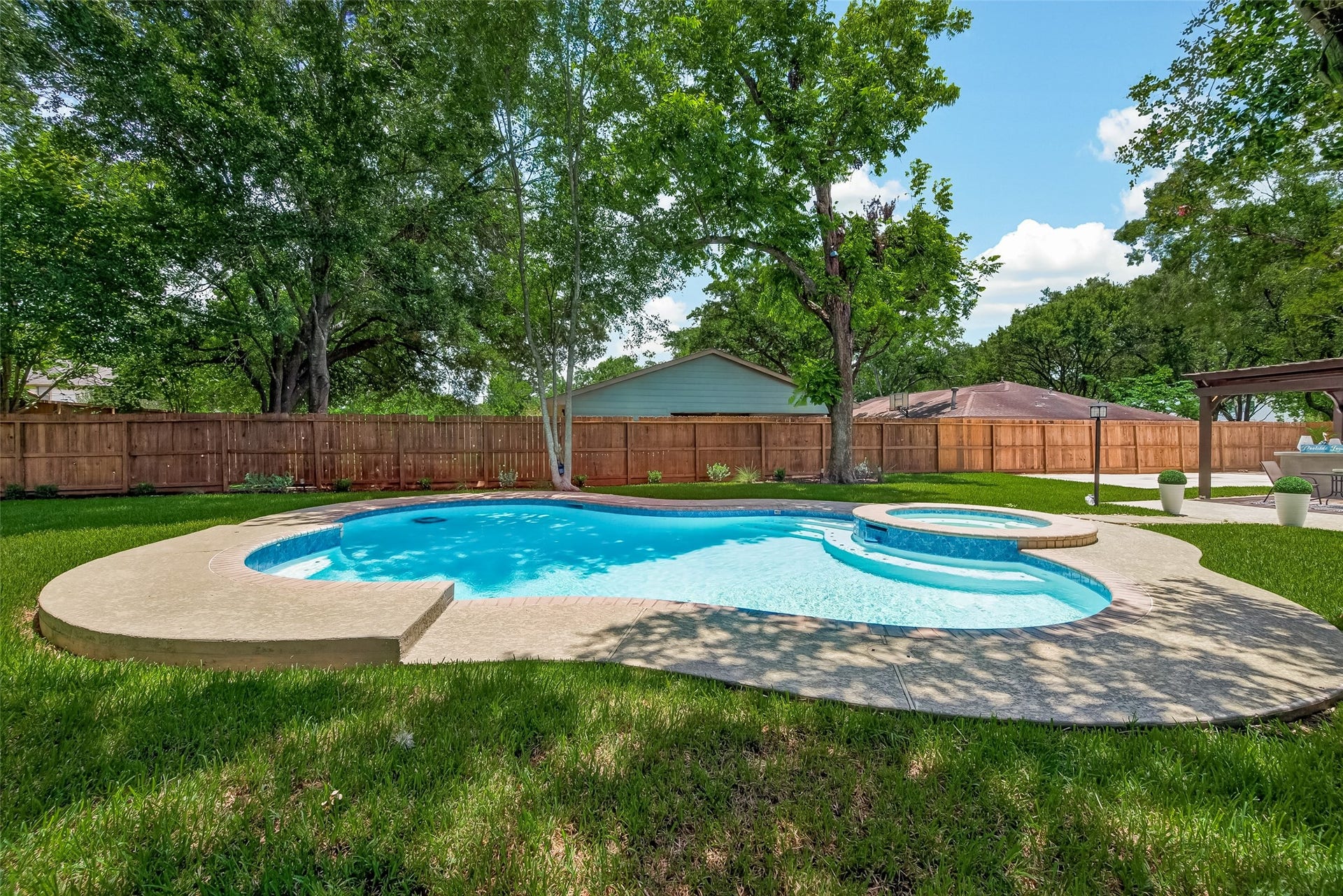 5422 Valerie Street, Bellaire, TX 77401 This backyard features a beautifully landscaped area with a sparkling pool and attached spa, surrounded by lush grass and mature trees, offering a private and relaxing outdoor retreat.