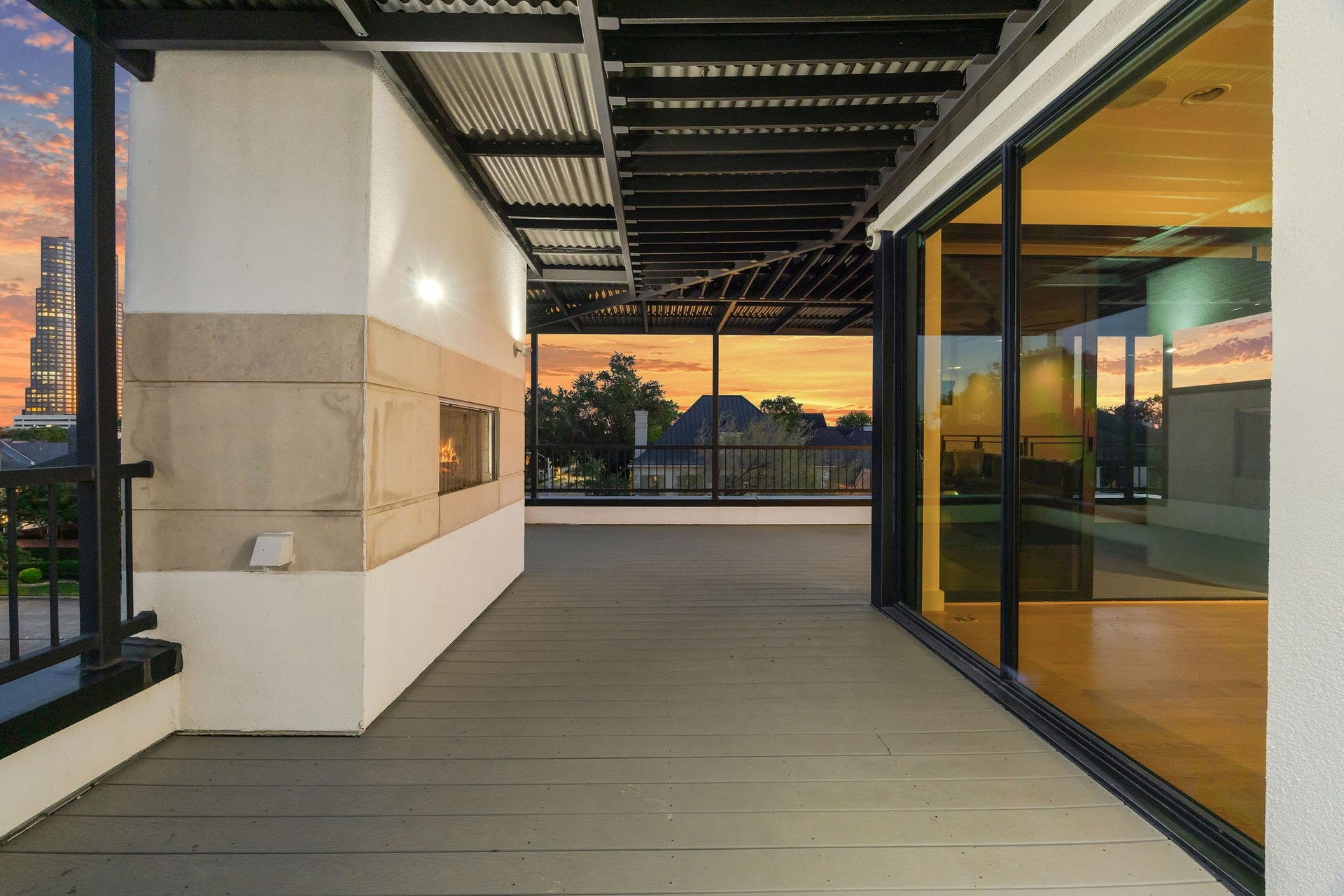 6002 Valley Forge Drive, Houston, TX 77057 Spacious terrace with a modern fireplace, sleek metal overhang, and expansive glass doors offering stunning sunset views.